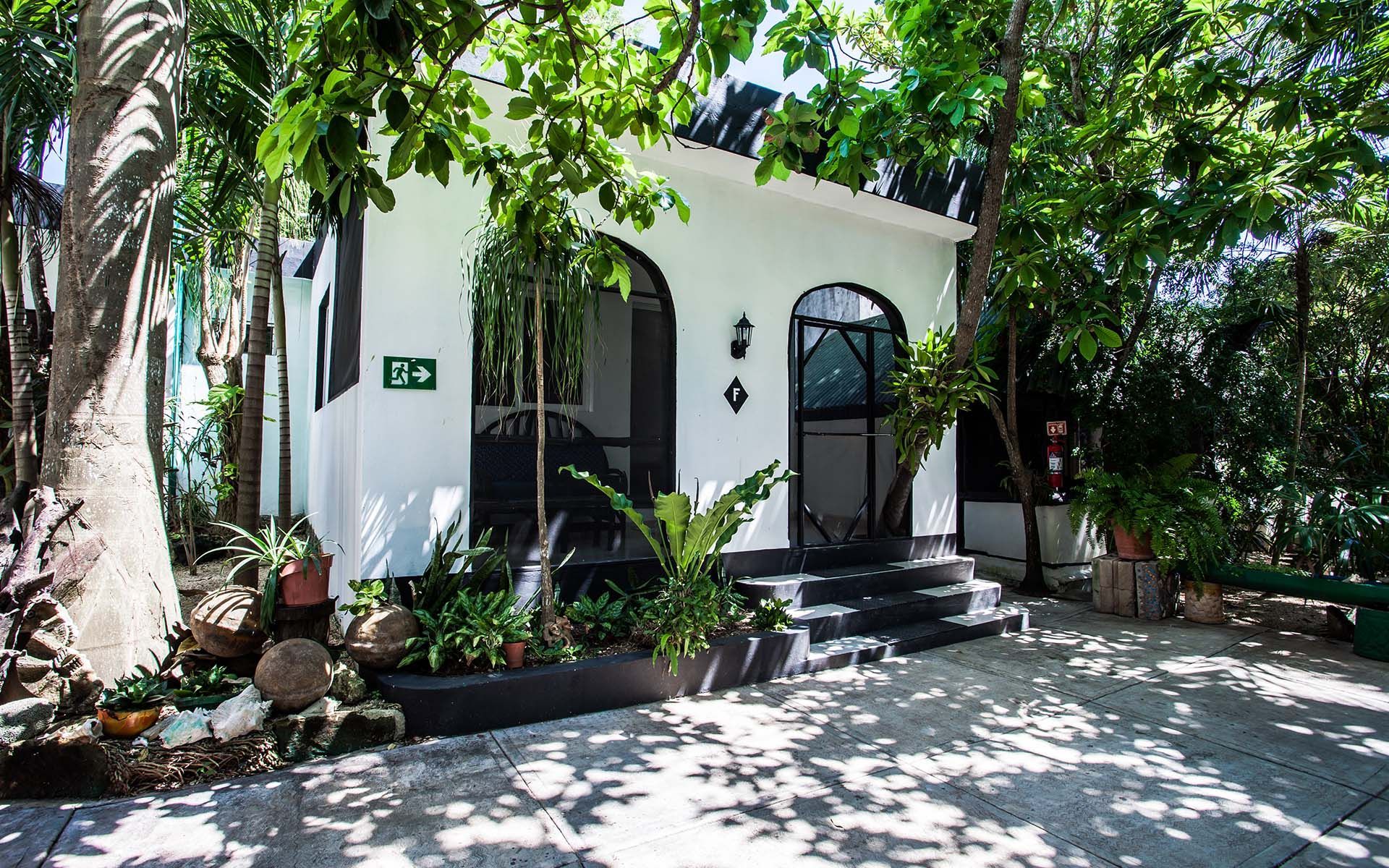 Edificio blanco con puerta arqueada y molduras negras, rodeado de árboles y vegetación.