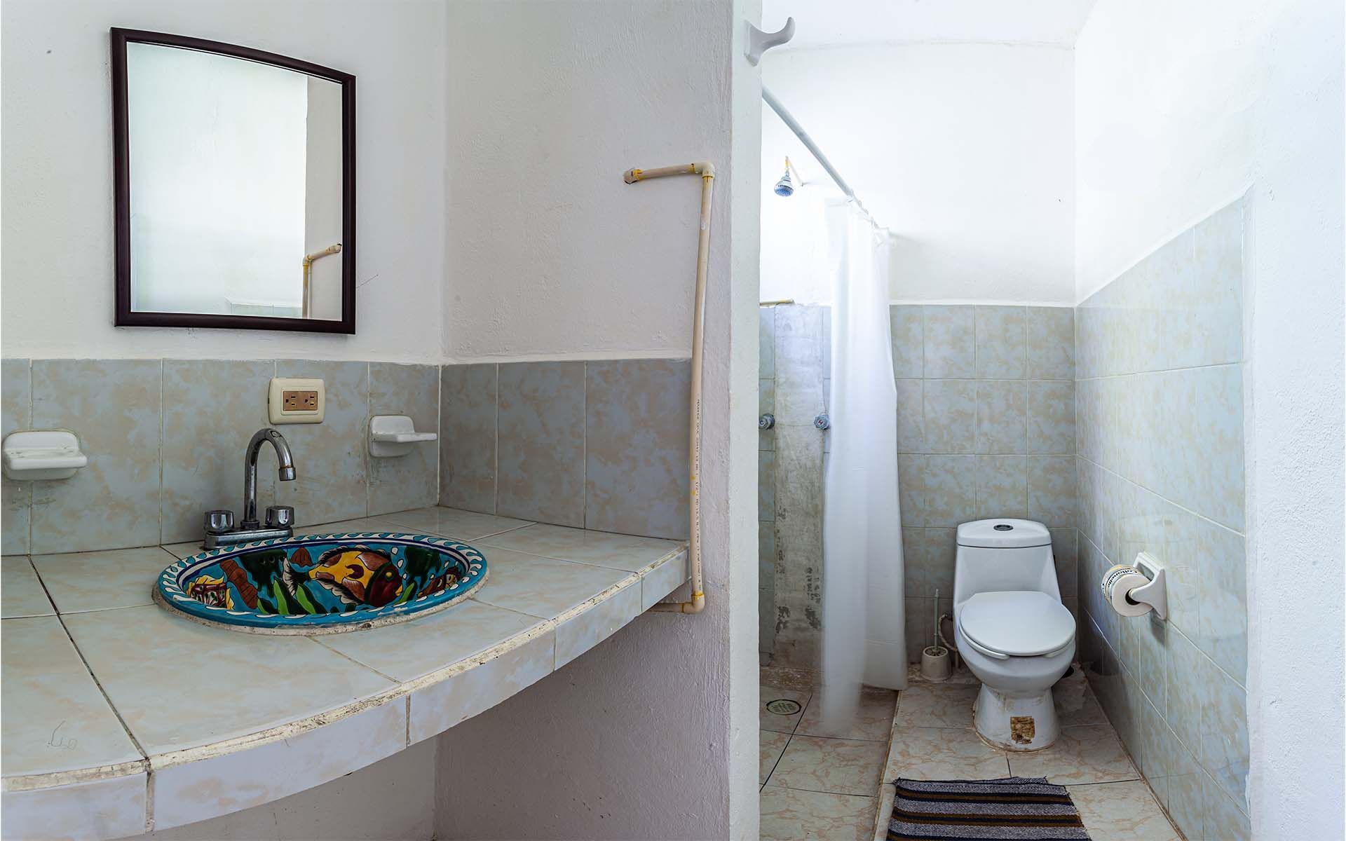 Baño con lavabo, espejo, inodoro y ducha. Azulejos grises y blancos, lavabo azul.