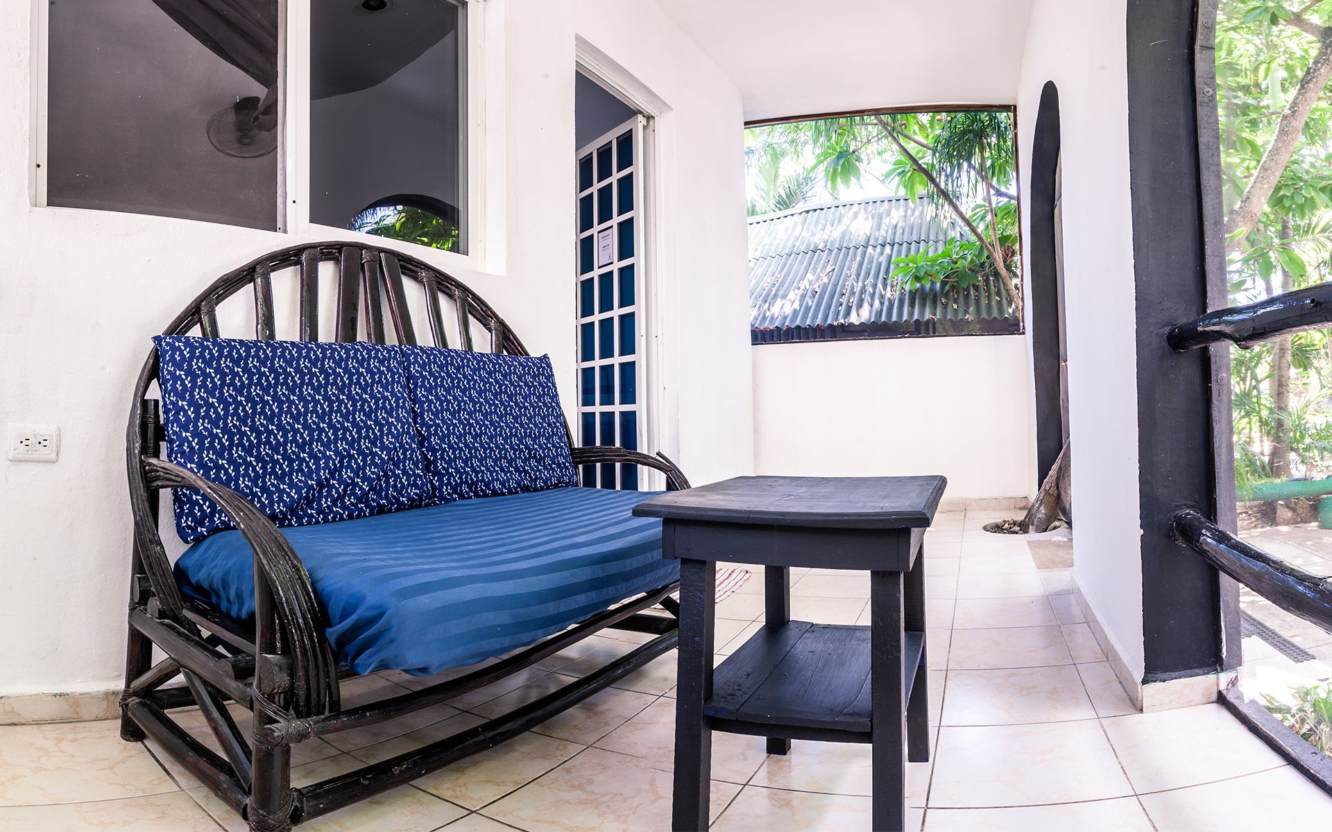 Zona de estar al aire libre con un sofá azul, una pequeña mesa negra y vistas a los árboles.