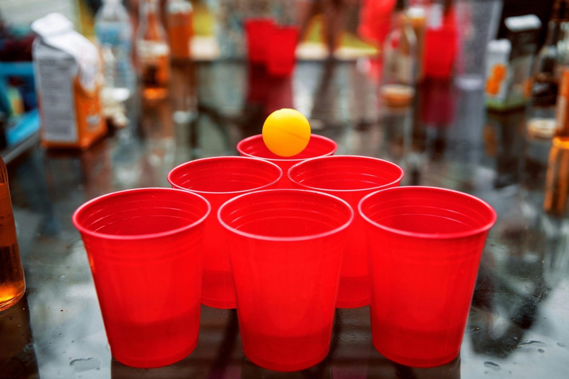 Vasos de plástico rojos preparados para jugar al beer pong, con una pelota amarilla rebotando en el centro.