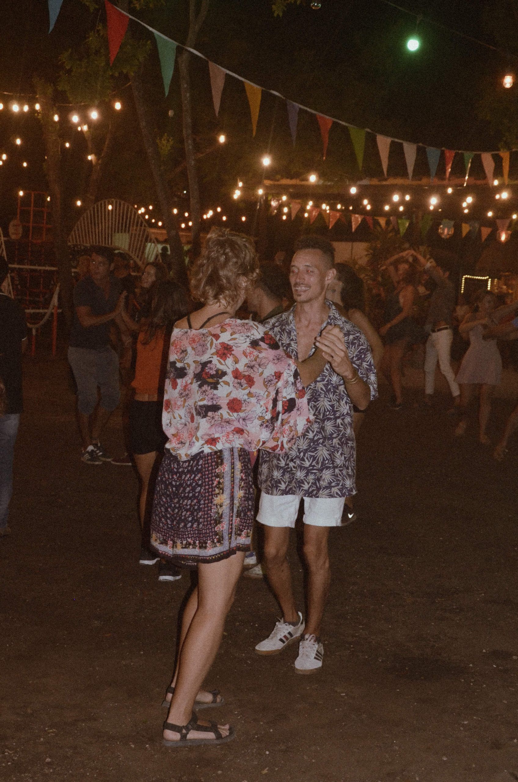 Dos personas bailando al aire libre por la noche bajo luces de cadena.