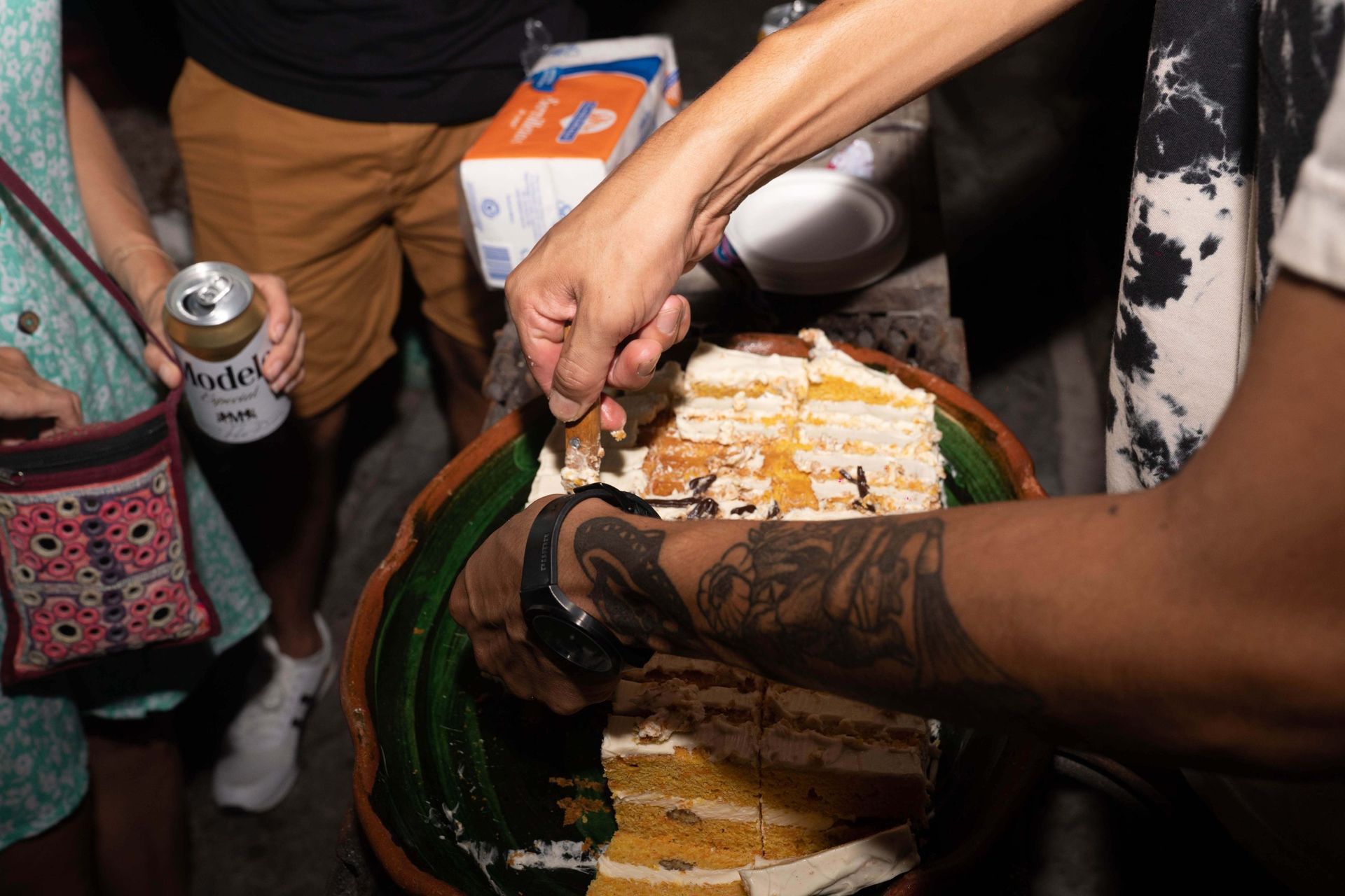 Personas cortando y compartiendo pastel de una bandeja decorativa en una reunión al aire libre.