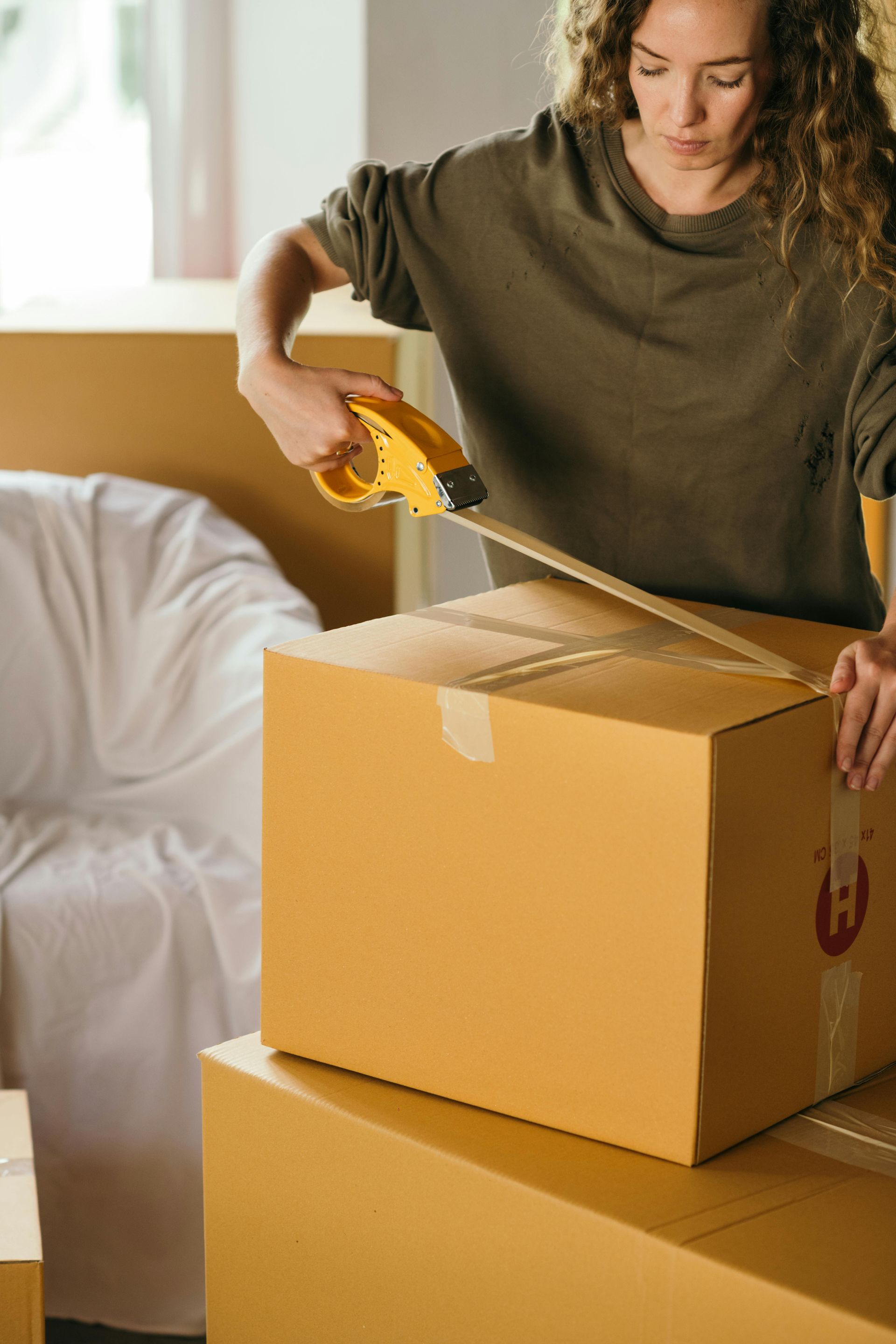 Woman sealing a cardboard box with packing tape, preparing for a move.