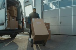 Delivery person unloading packages from a van using a dolly outside a loading dock.