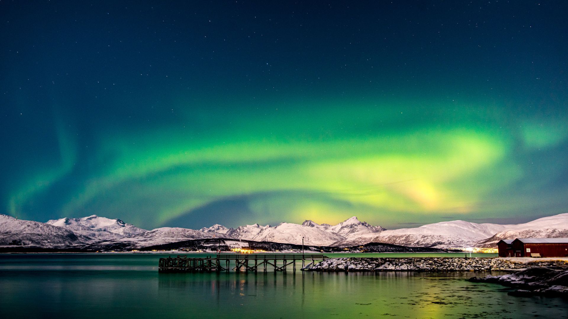 Northern lights illuminate a snowy mountain range over a calm lake.