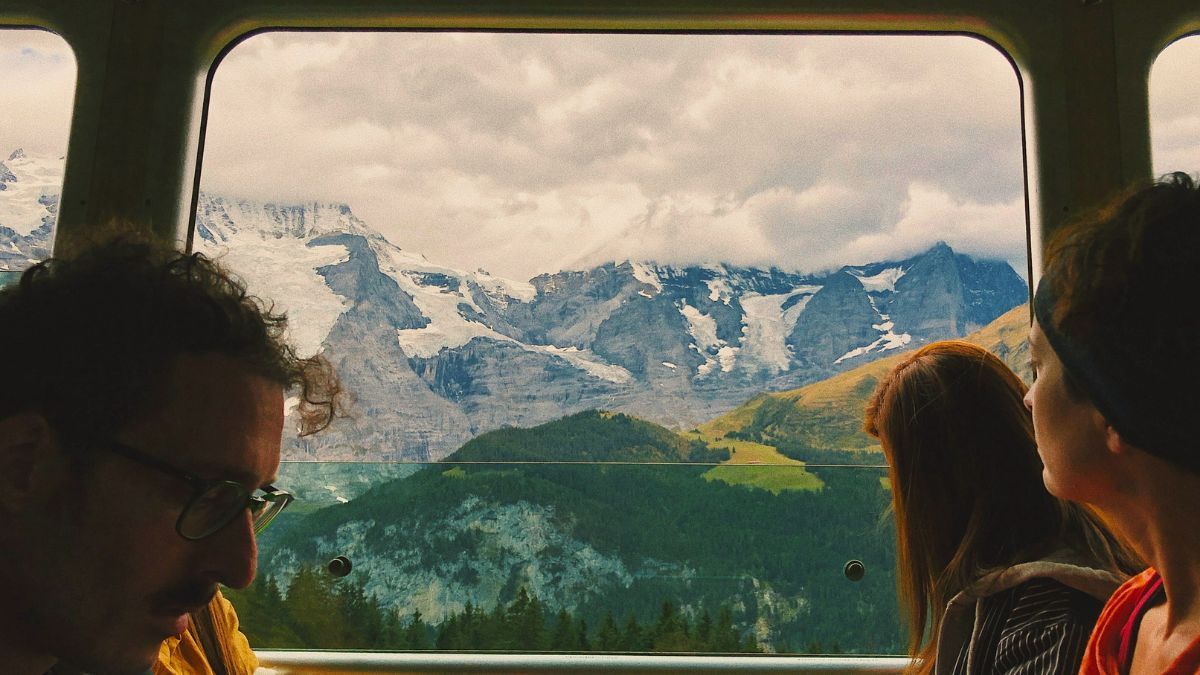 A group of people are looking out of a train window at mountains.