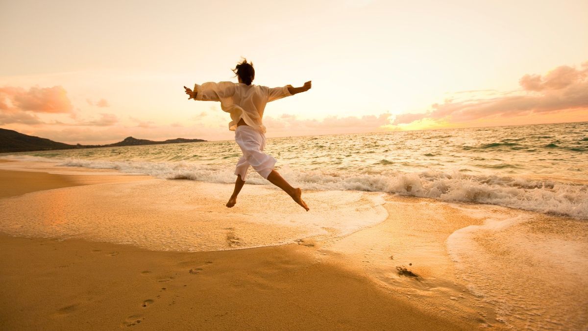 A woman is jumping in the air on a beach at sunset.