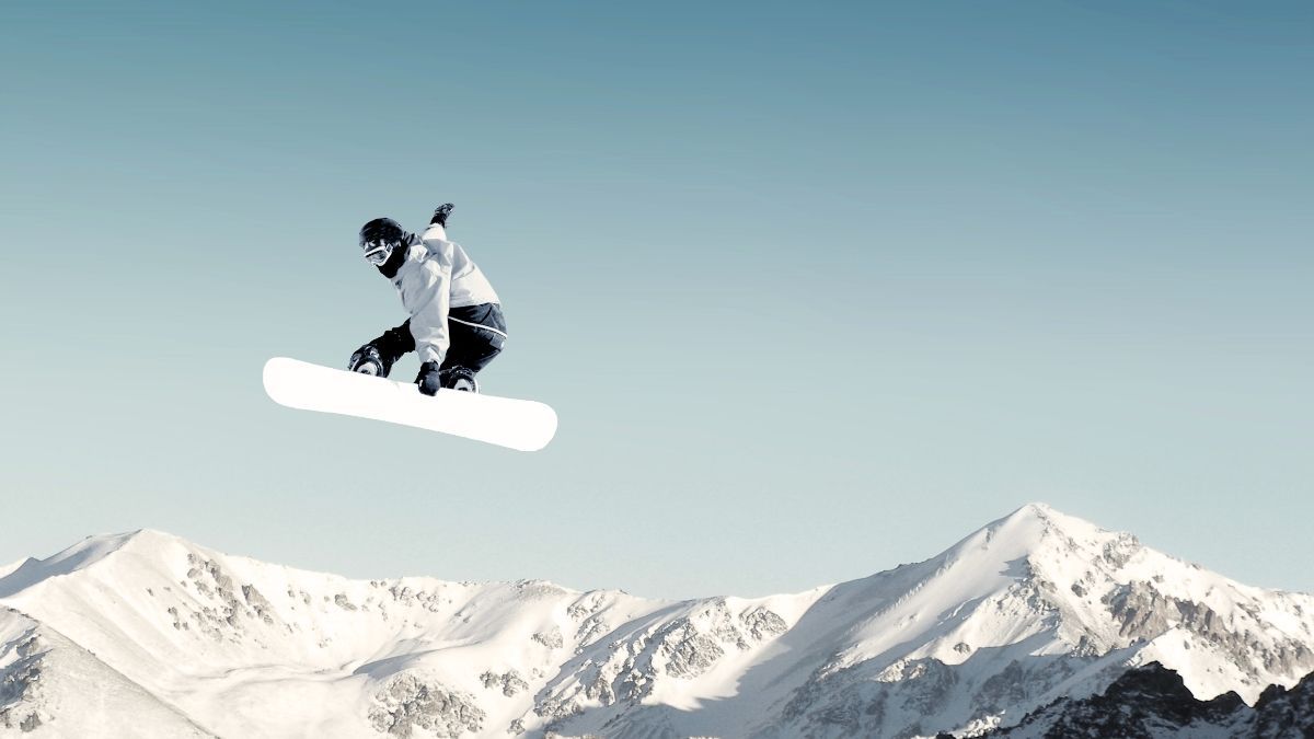 A snowboarder is jumping in the air over a snowy mountain.