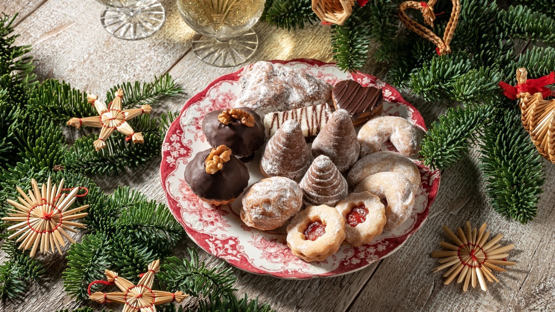 Plate of Christmas cookies with champagne and festive evergreen decorations.