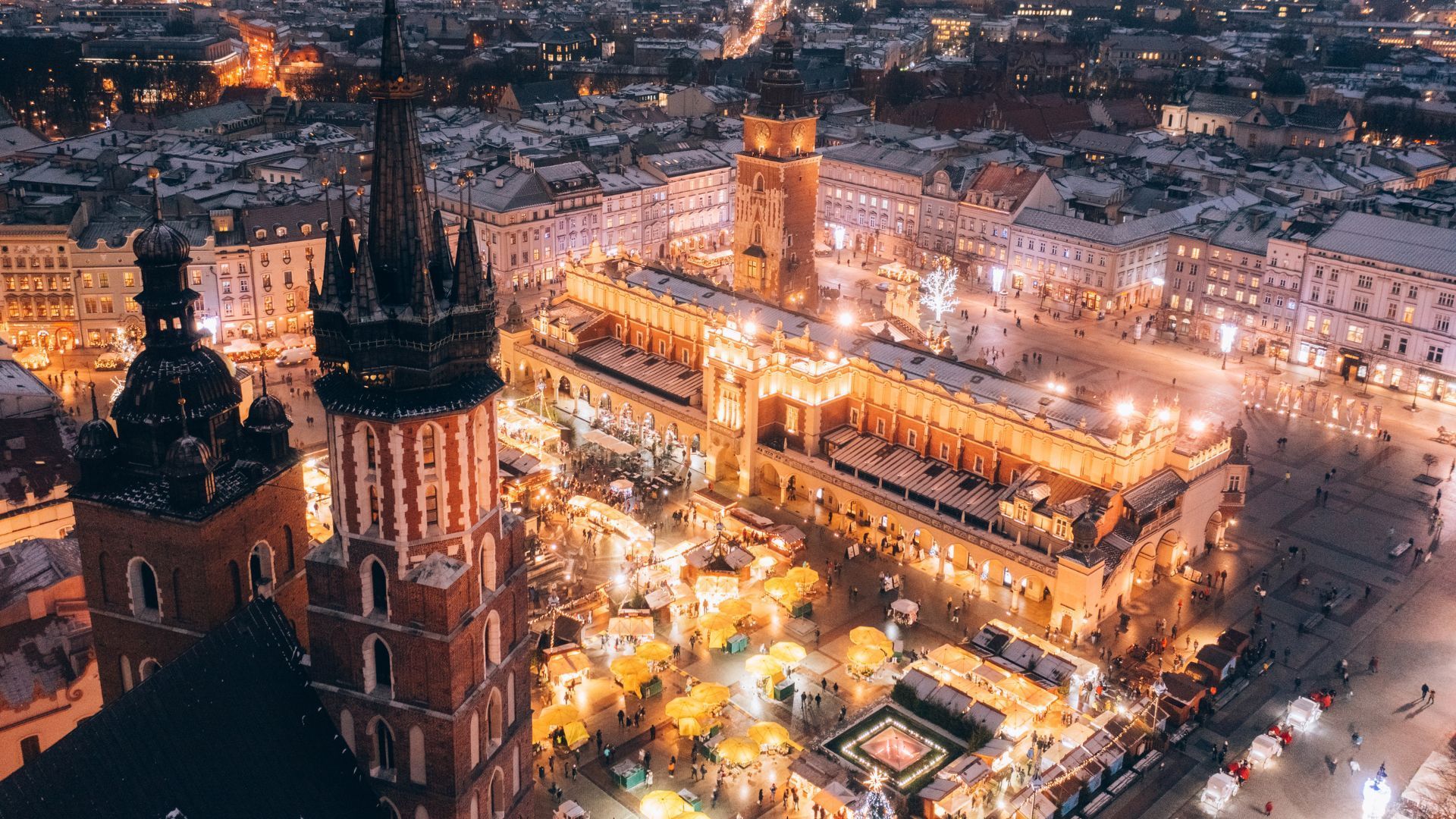 Night aerial view of Kraków's Main Market Square, illuminated with lights, featuring the Cloth Hall and St. Mary's Basilica.