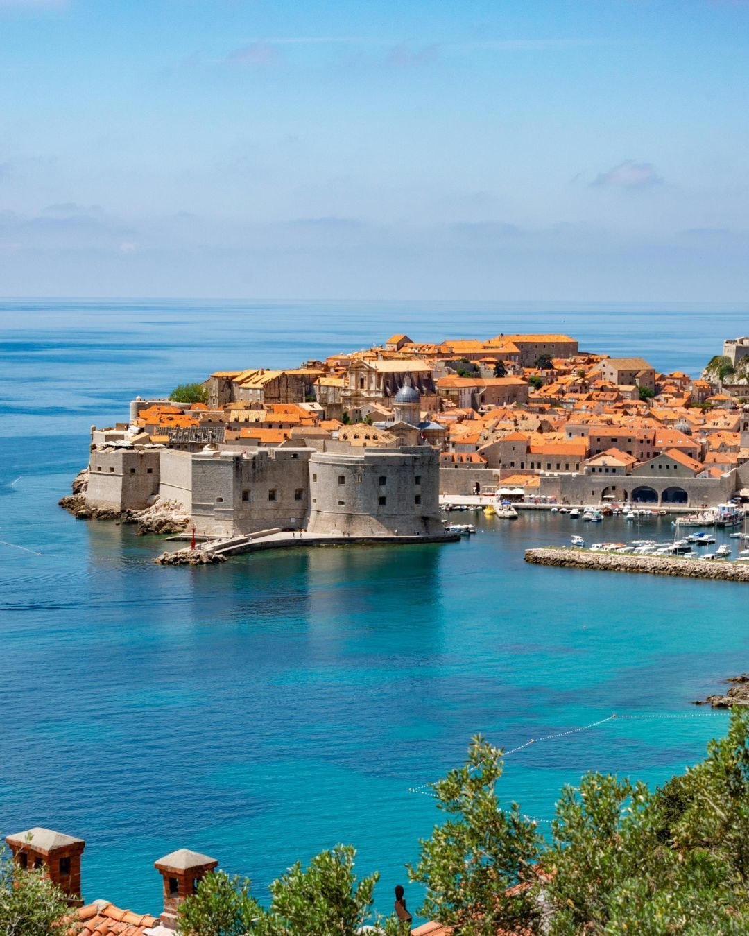 Coastal old town with orange roofs on a rocky peninsula beside clear blue sea and harbor.