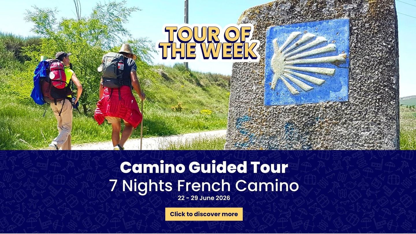 Two hikers walk along a path next to a stone marker bearing the blue and white scallop shell symbol of the Camino.
