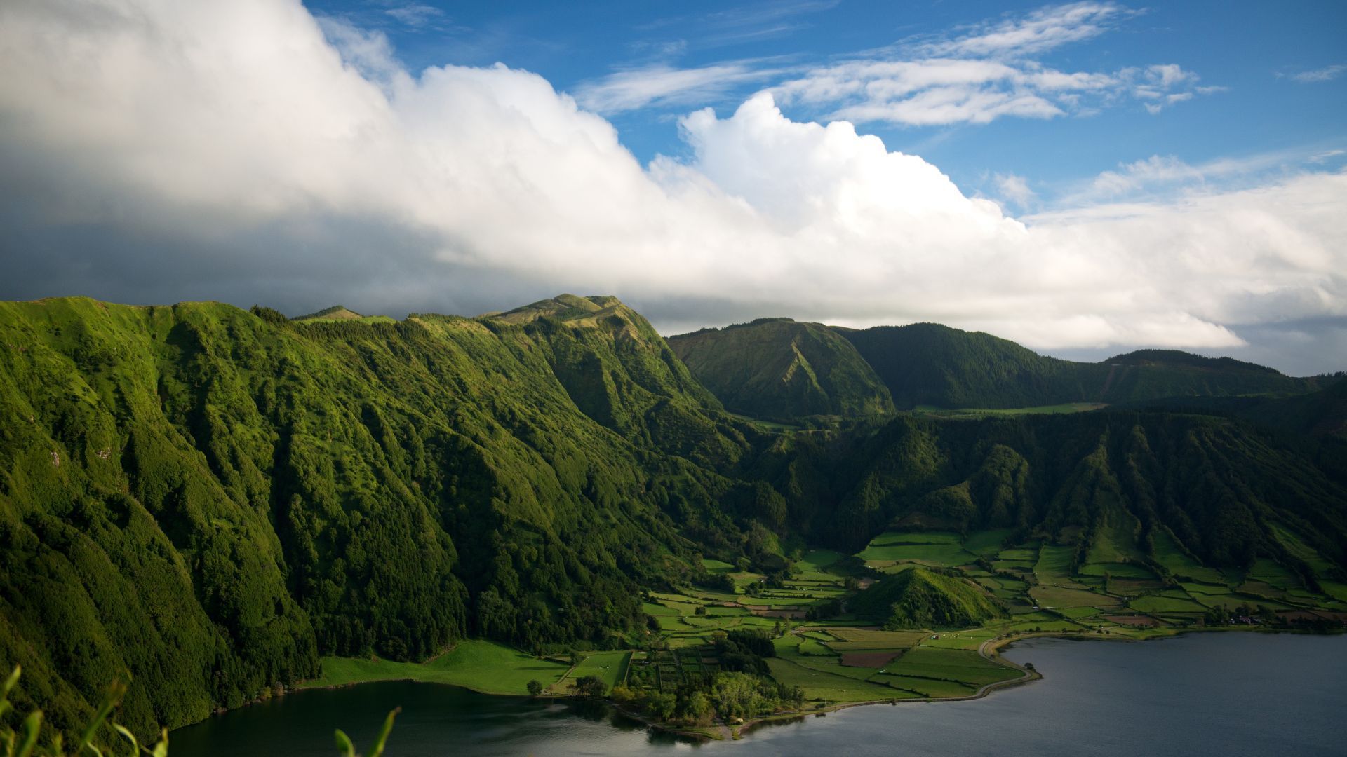 A view of a lake surrounded by mountains on a cloudy day in Azores.