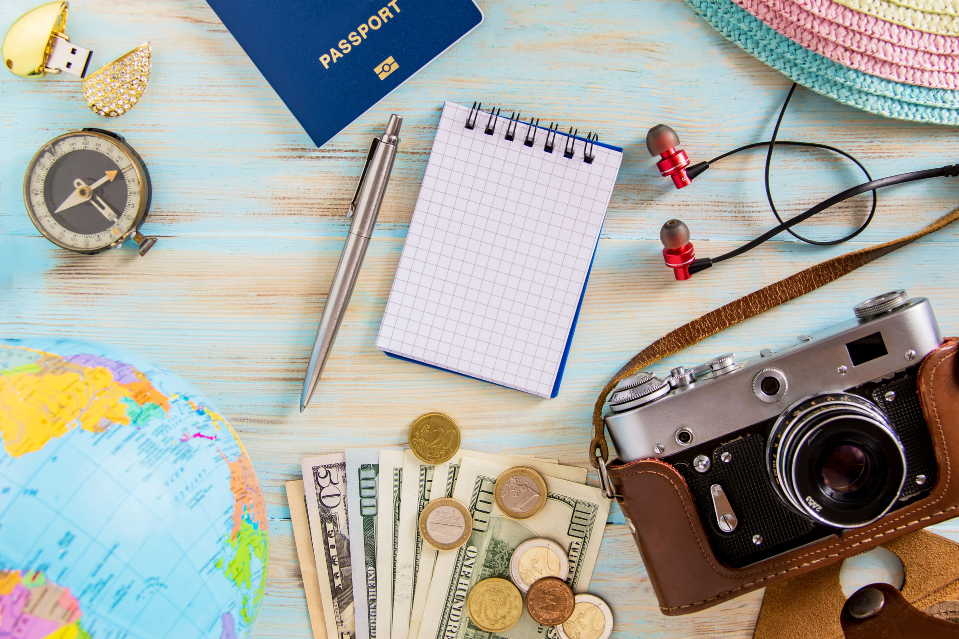 Table with items you would bring travelling. camera, earphones, compass
, globe, notepad, money pen, notebook
