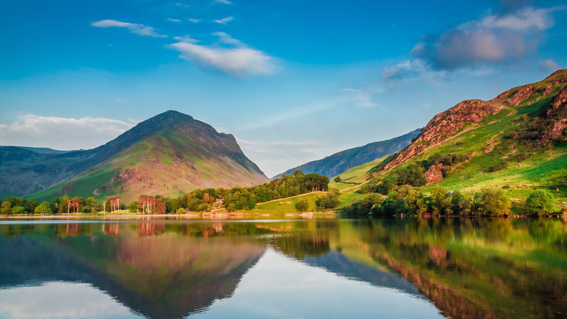 The Lake District surrounded by mountains and trees with mountains reflected in the water.