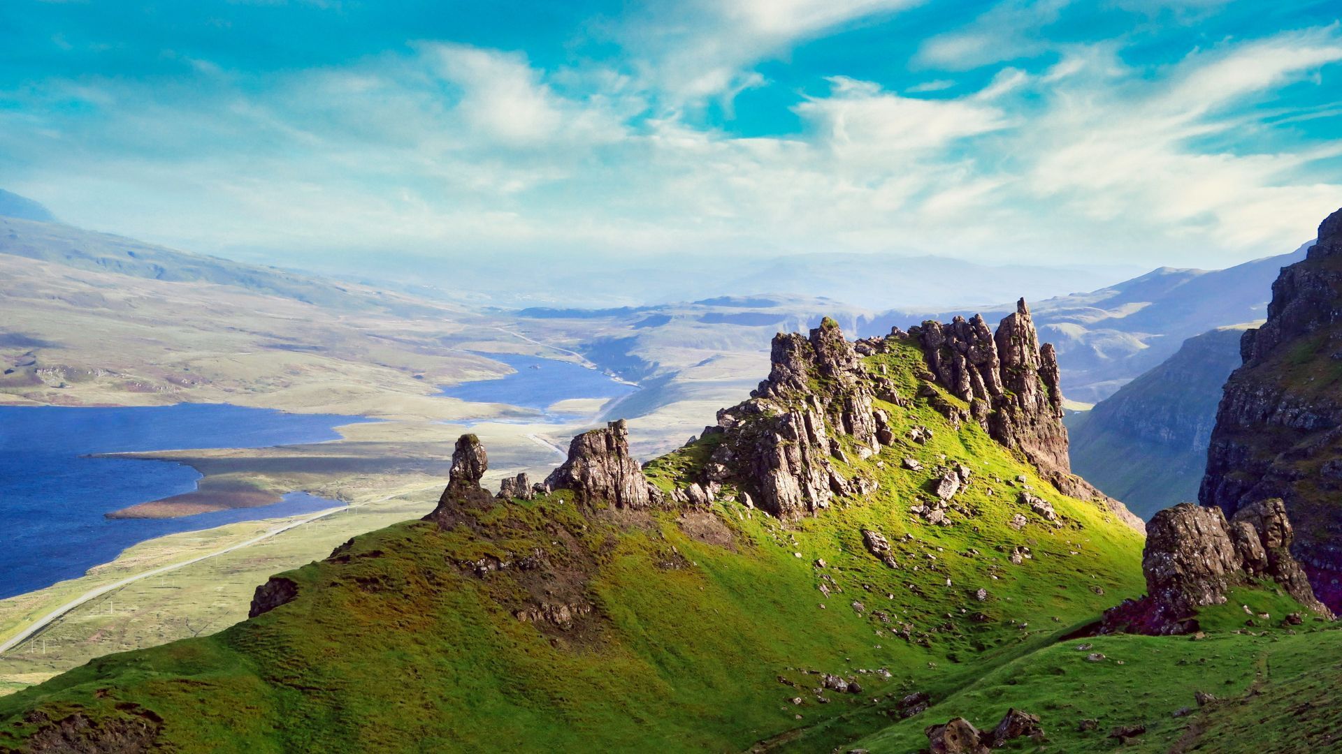 A mountain covered in grass and rocks with a lake in the background.