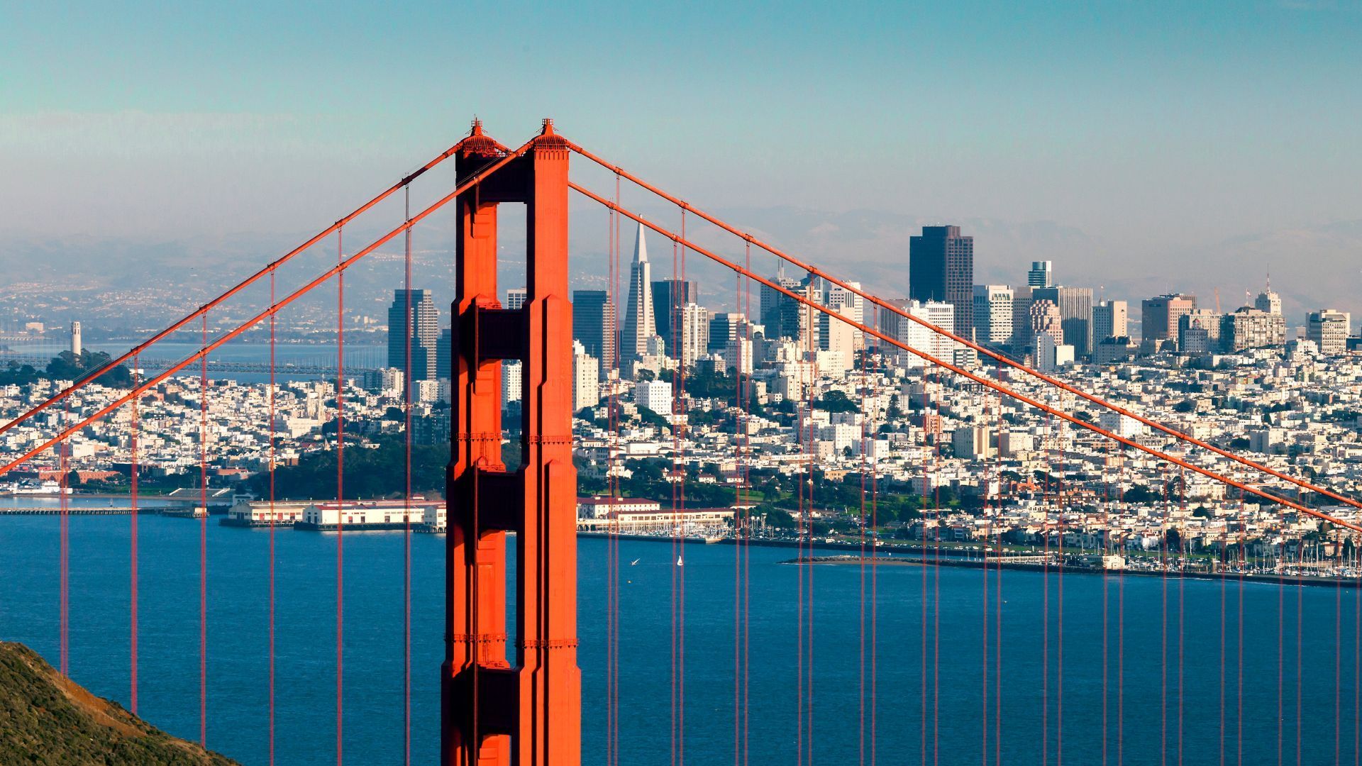 the Golden Gate Bridge over a body of water with a city in the background.