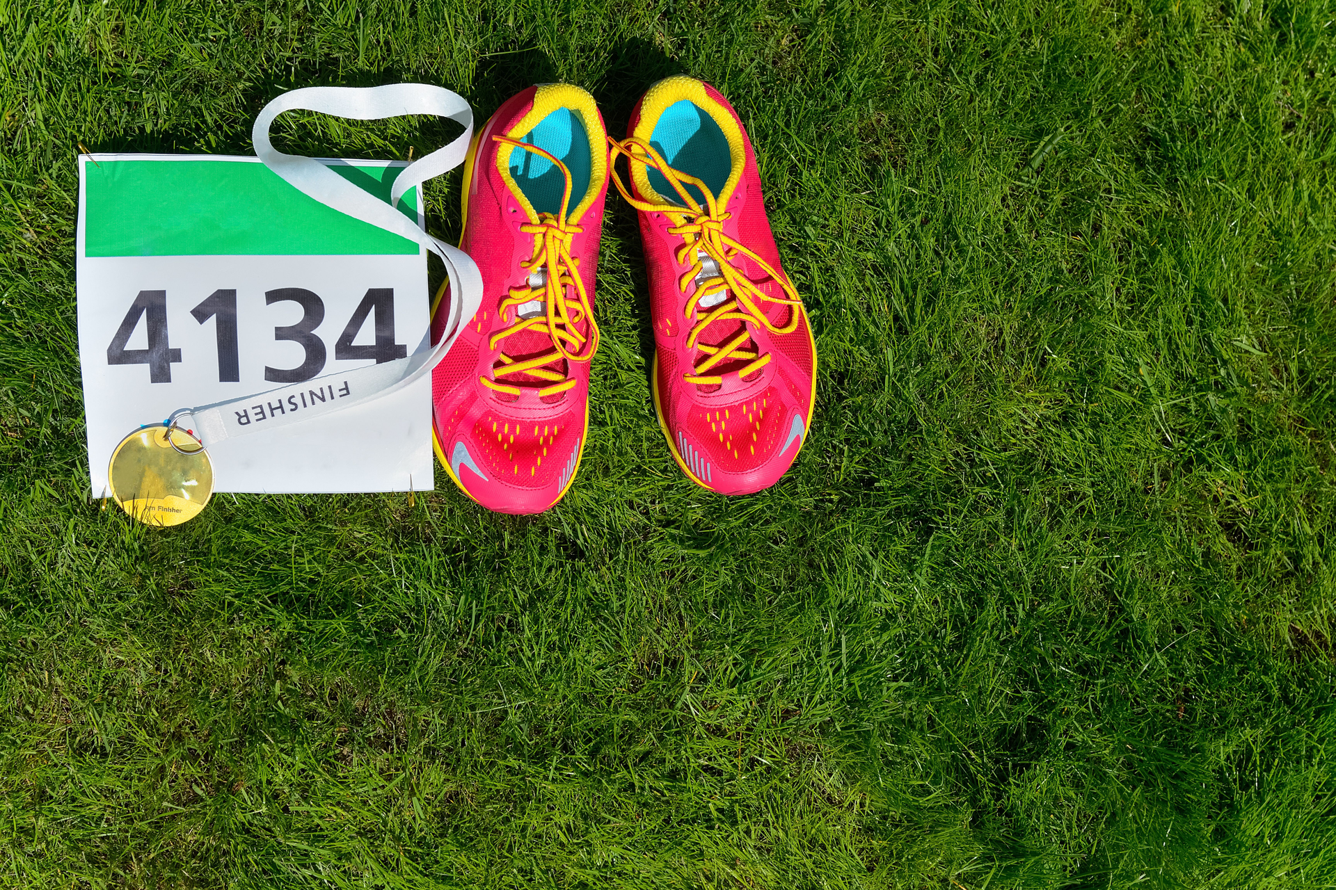 A pair of running shoes, with a marathon number and medal on grass