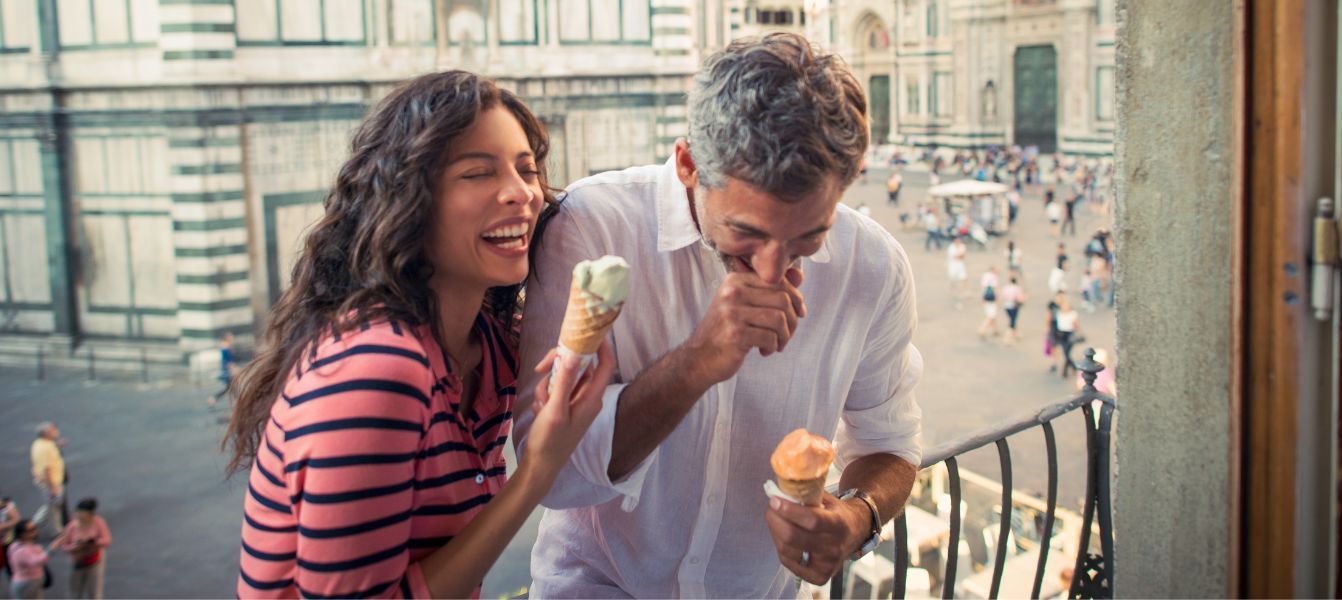 A man and a woman are eating ice cream on a balcony.