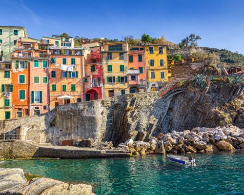 A row of colorful buildings on a cliff overlooking a body of water.