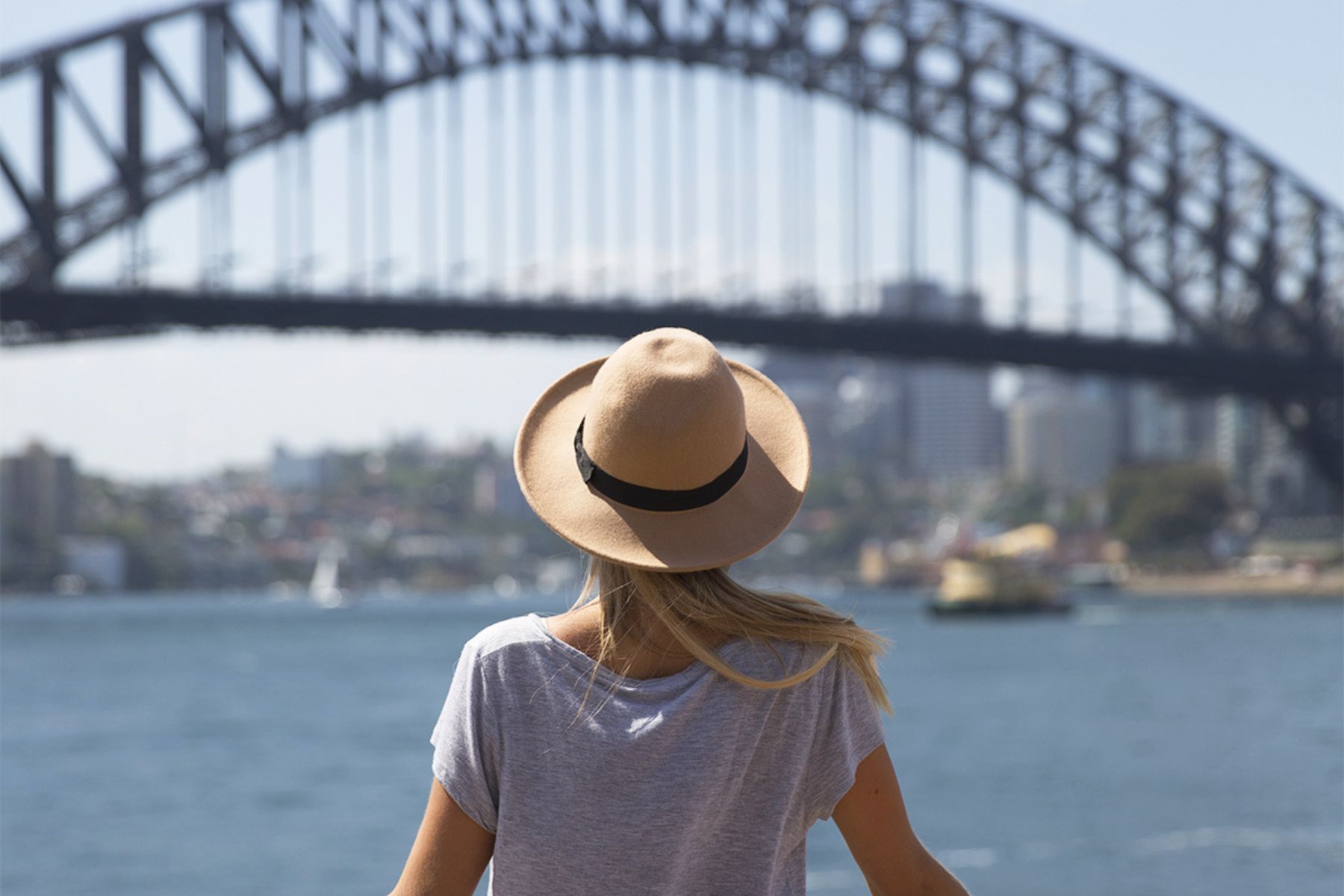 Contiki Australia A woman in a hat is standing in front of a bridge over a body of water Barters Travelnet