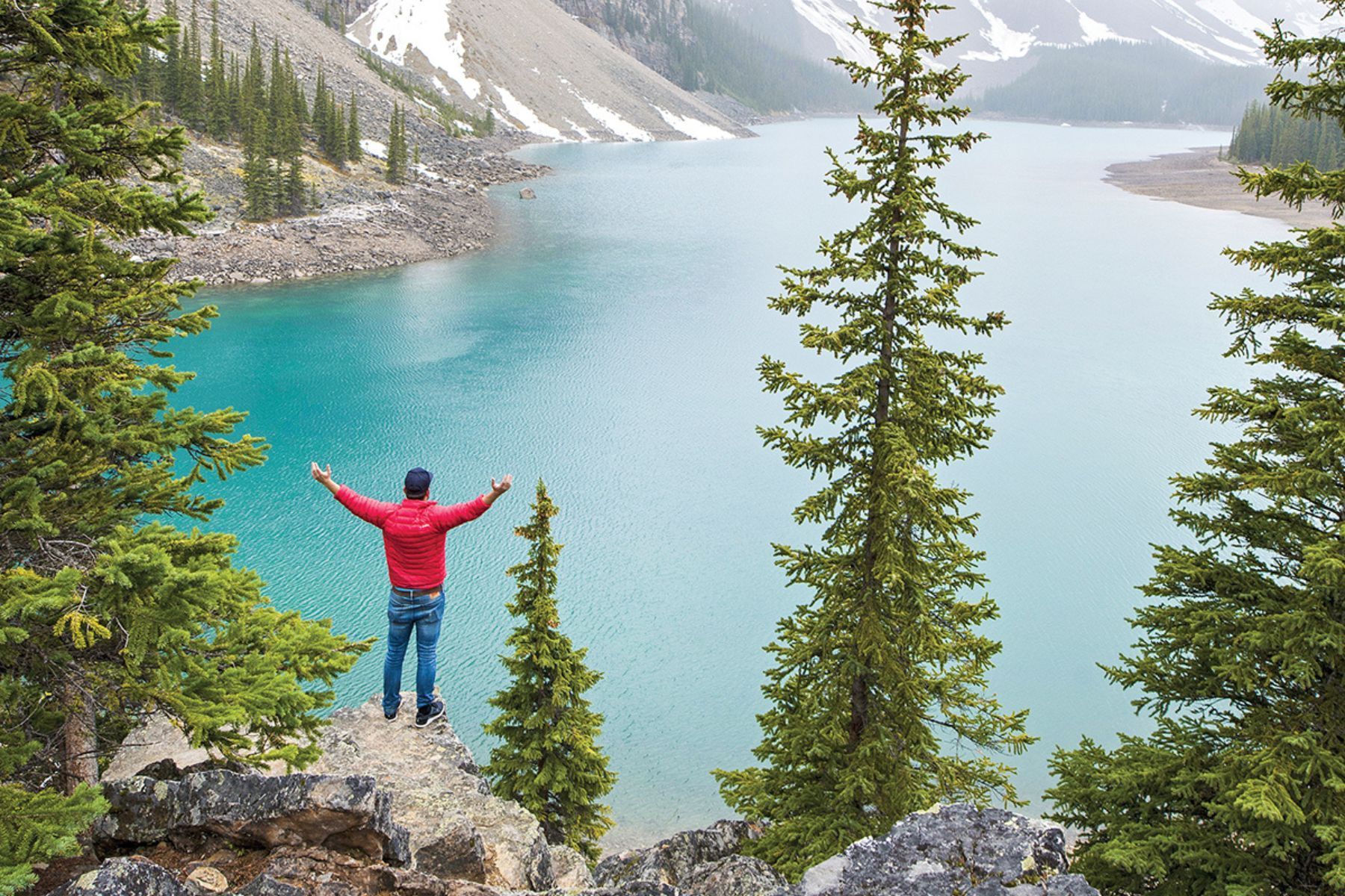 Contiki USA and Canada A man is standing on a cliff overlooking a lake with his arms outstretched Barters Travelnet