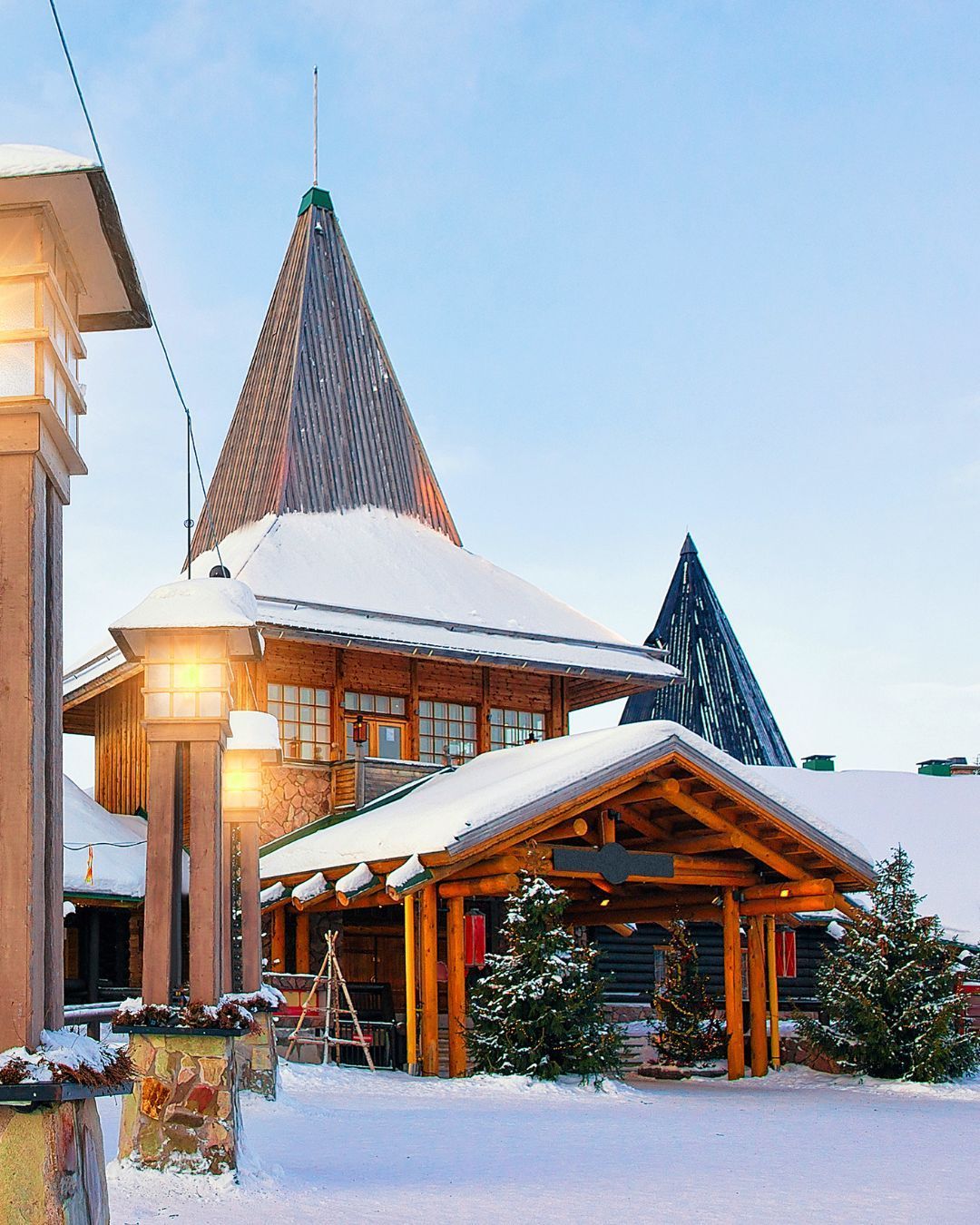 Snow-covered chalet with lit porch and tall peaked roof at dusk