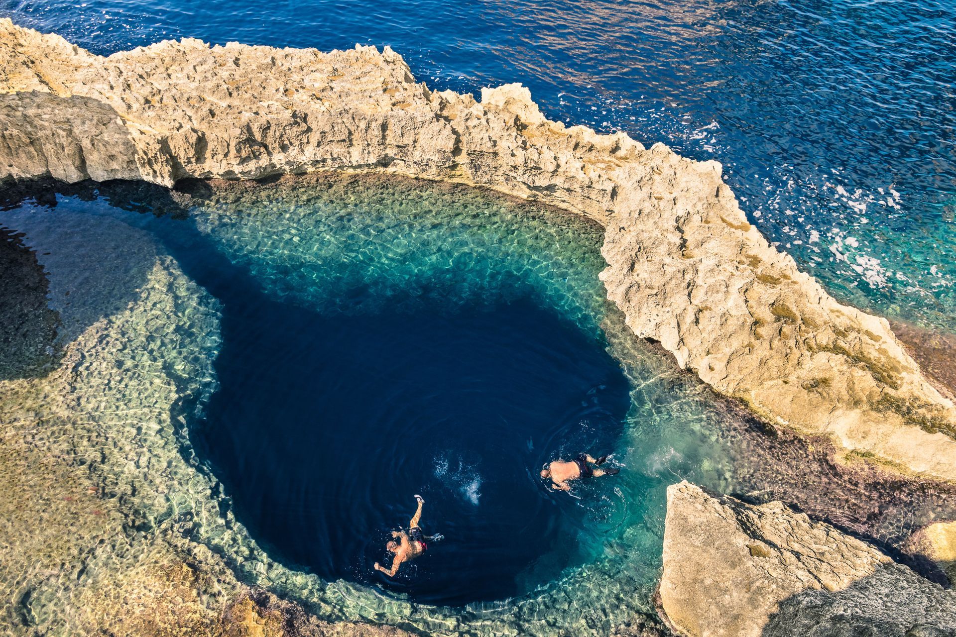 People swimming on a beach in Malta surrounded by cliffs 