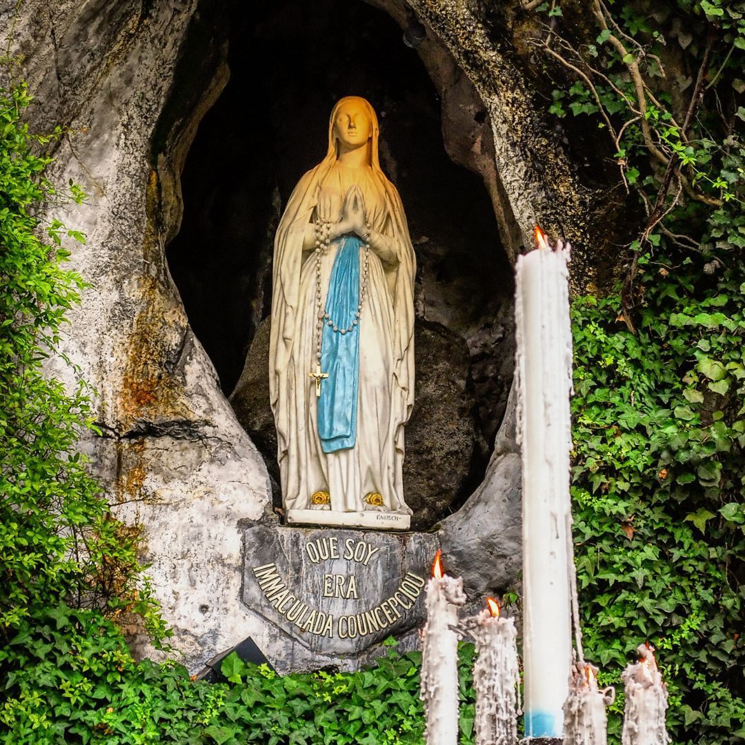 A statue of the Virgin Mary Massabielle in a cave with candles in Lourdes