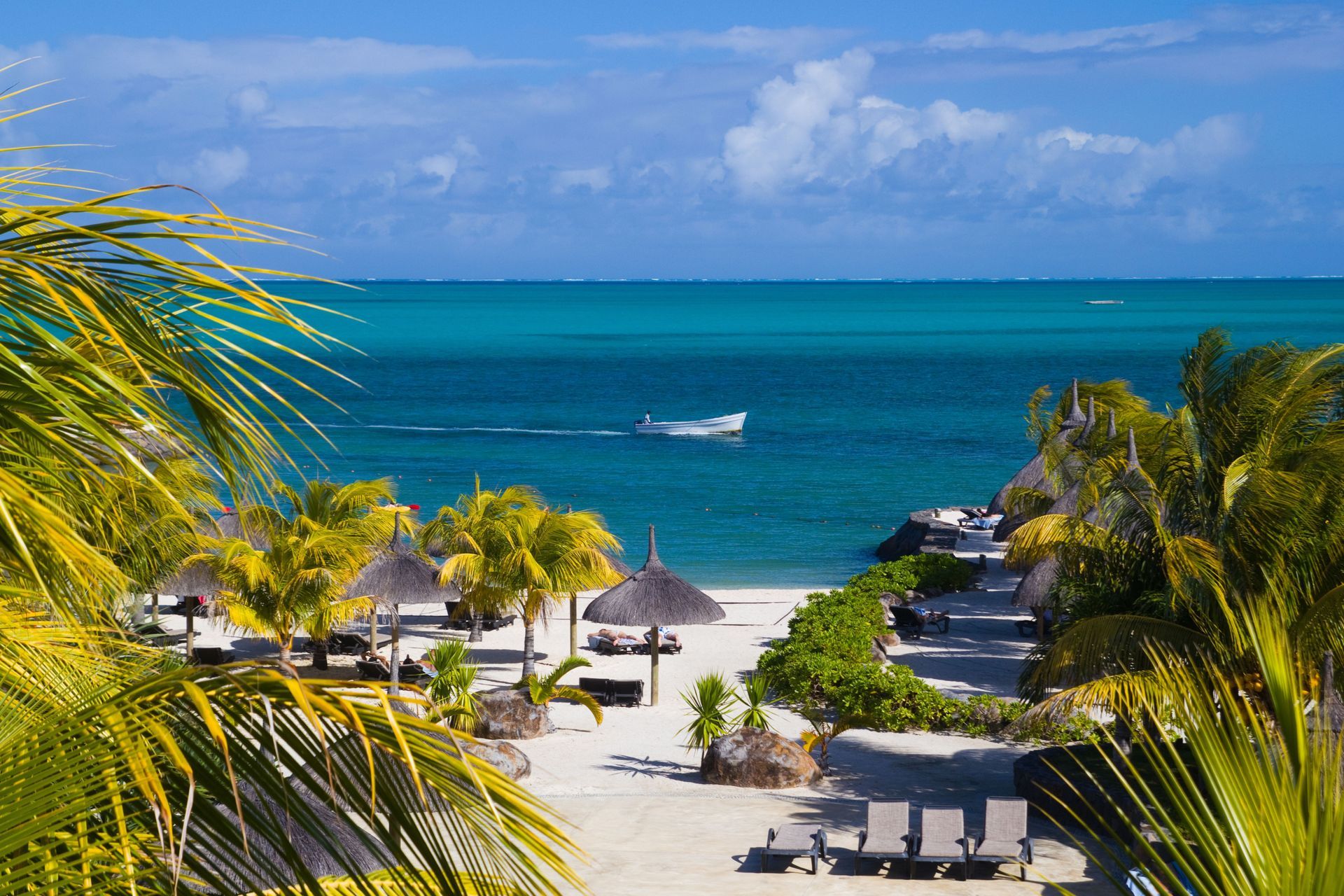 A beach with umbrellas and chairs and a boat in the ocean