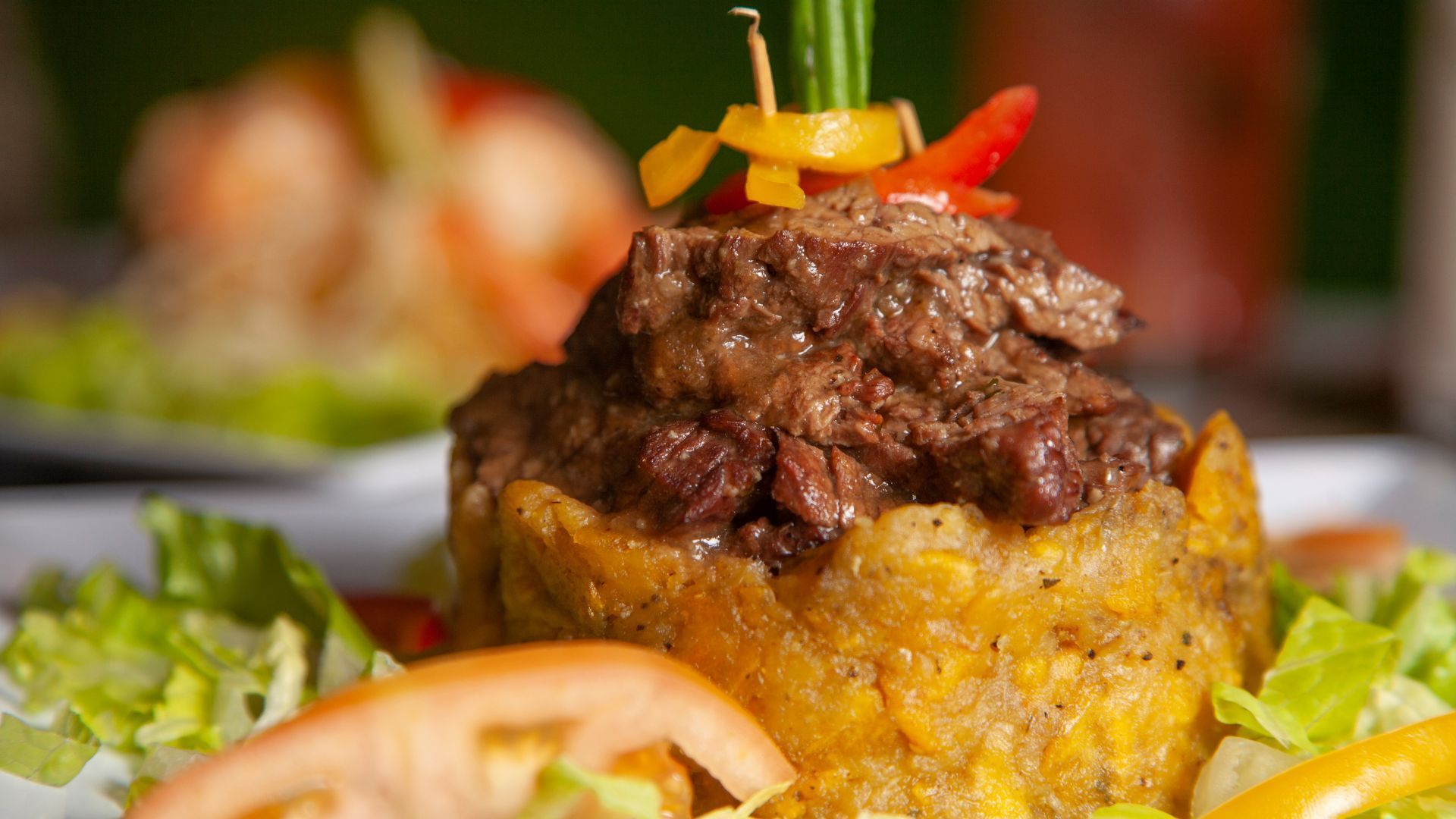 Mofongo topped with steak and peppers, garnished with lettuce and tomato slices.