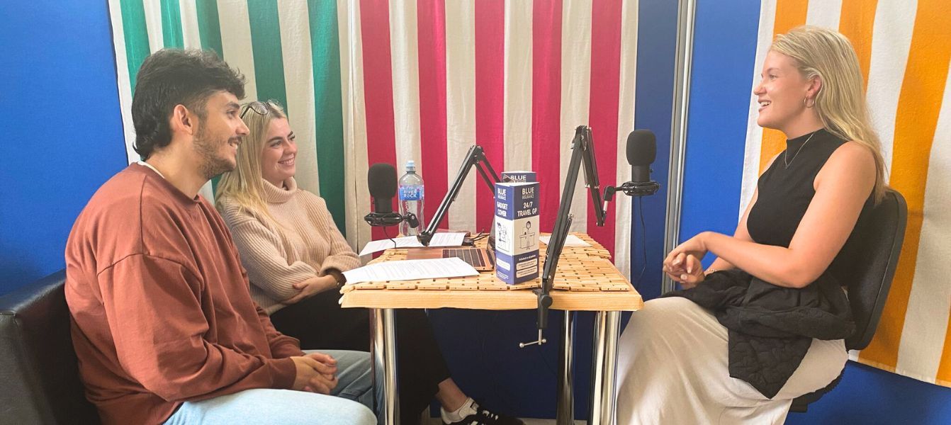 A man and a woman are sitting at a table in front of a microphone.