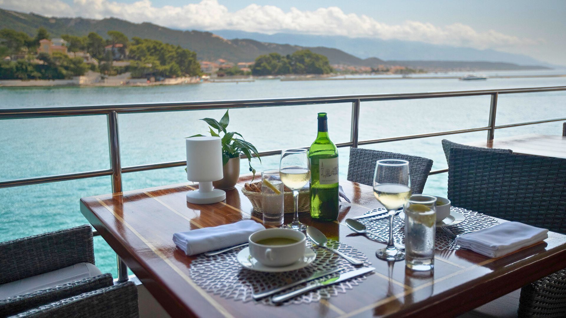 A table with a bottle of wine and glasses on it overlooking the ocean.