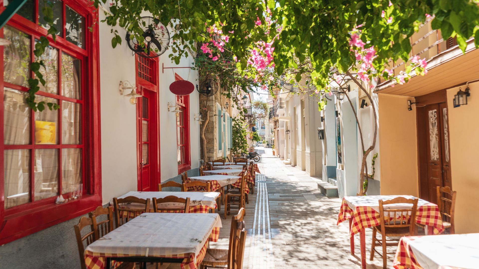 A row of tables and chairs outside of a restaurant on a narrow quiet street in Nafplion, Greece