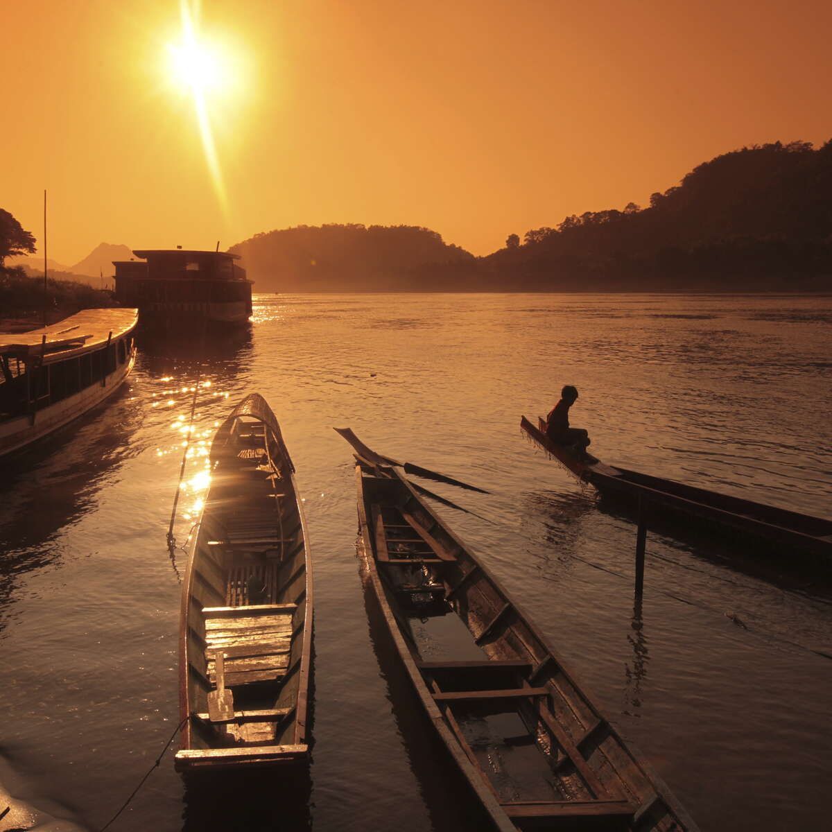 A man sits in a boat on a river at sunset