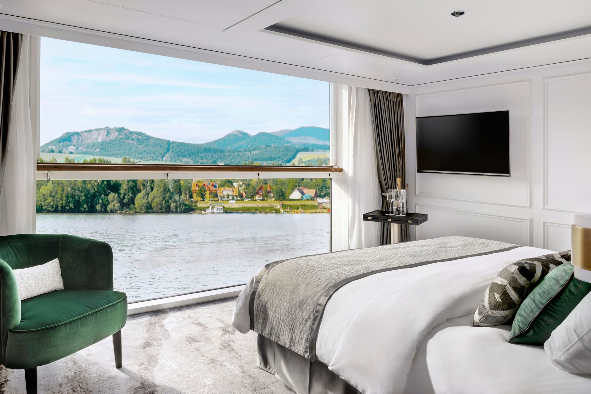 Stateroom with a bed , chair , television and a view of a lake.