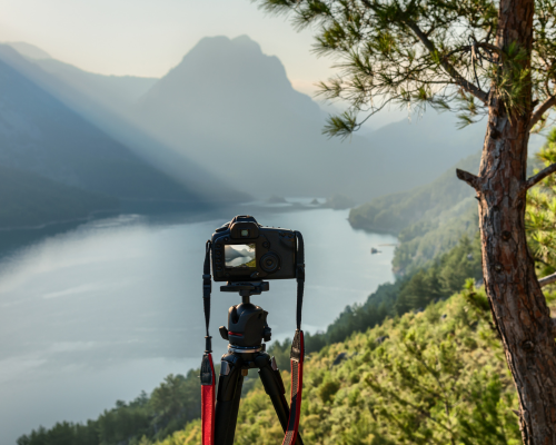 A camera on a tripod is taking a picture of a lake in the mountains.