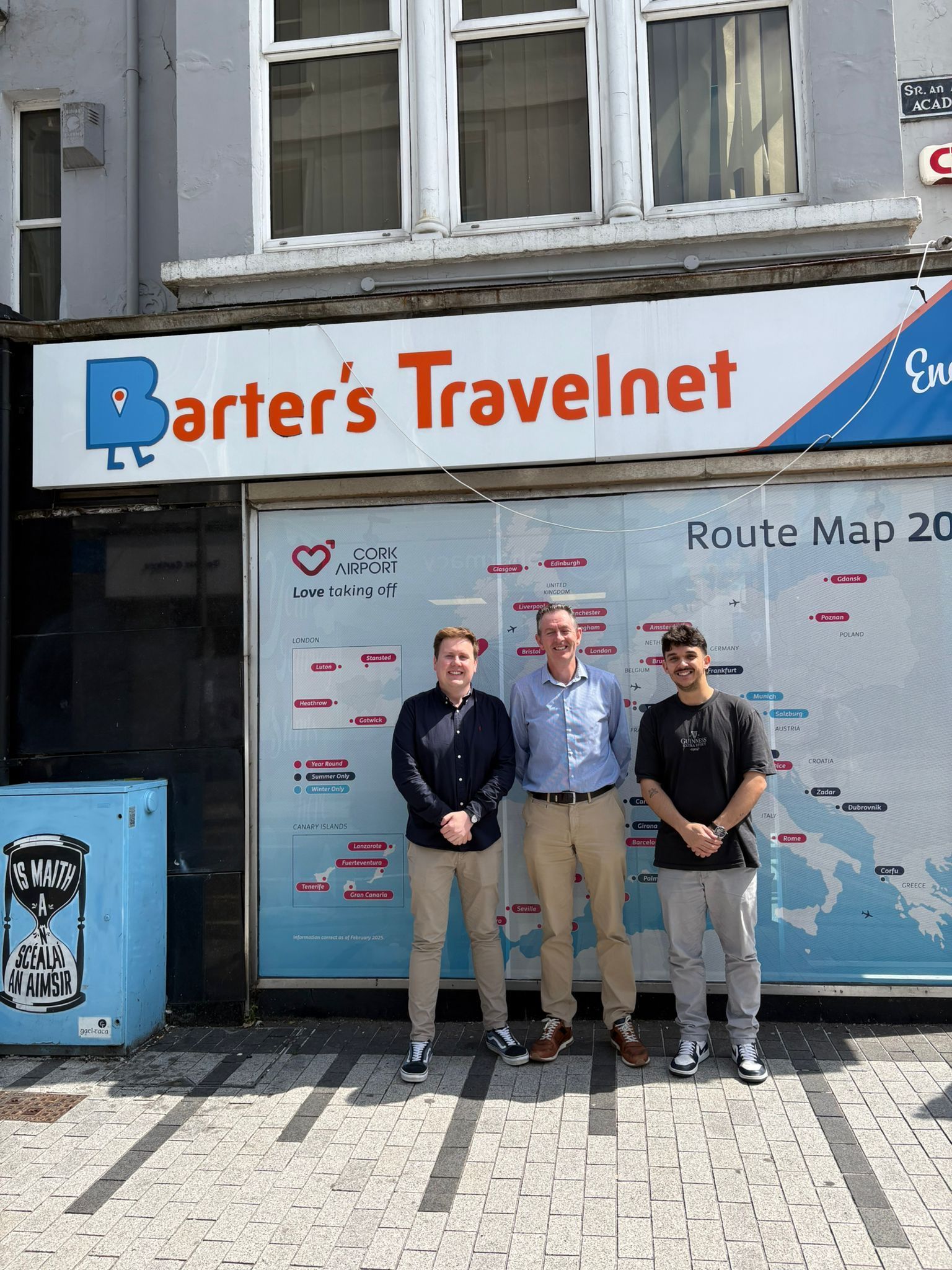 Three men stand in front of a closed travel agency with a 