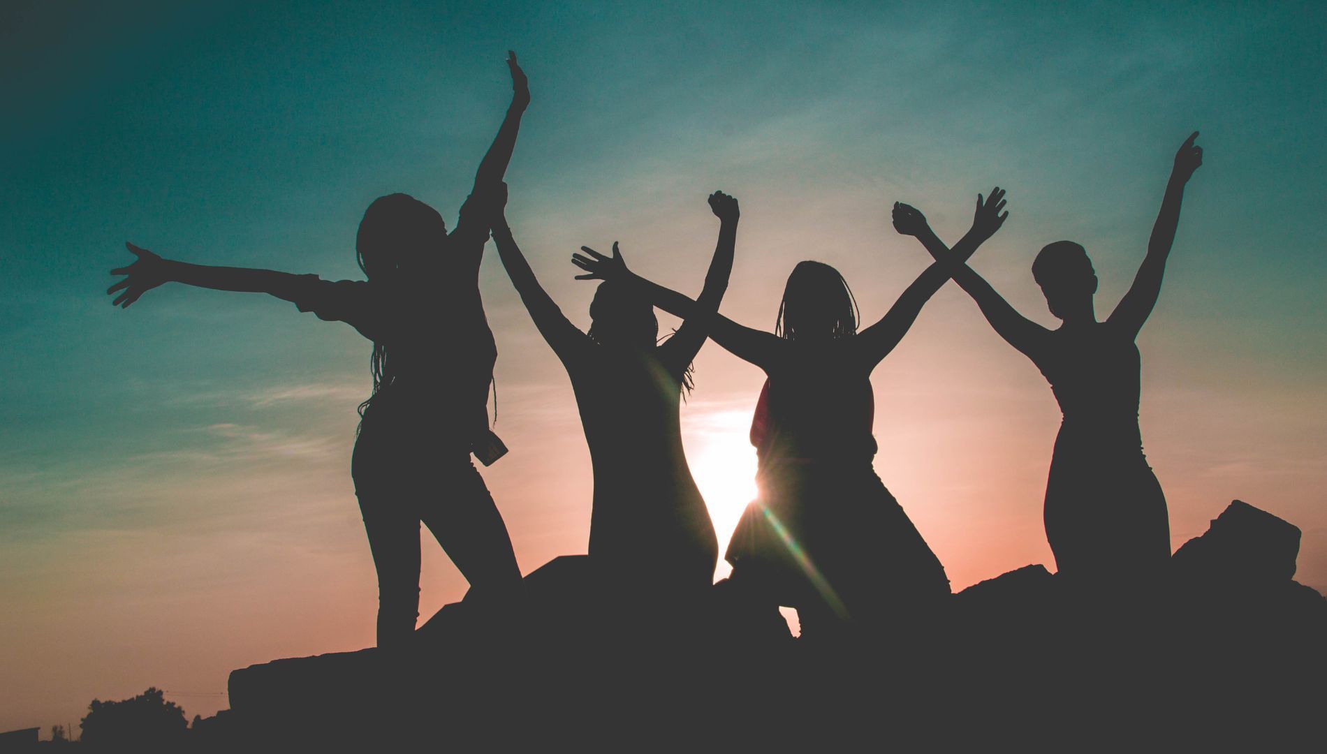 A group of women are standing on top of a hill with their arms in the air