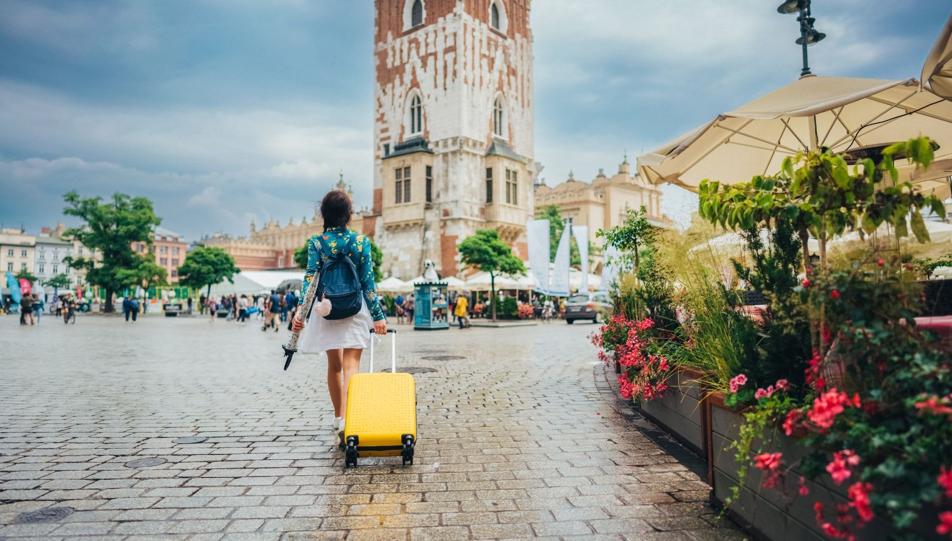 A woman is pushing a yellow suitcase down a cobblestone street.