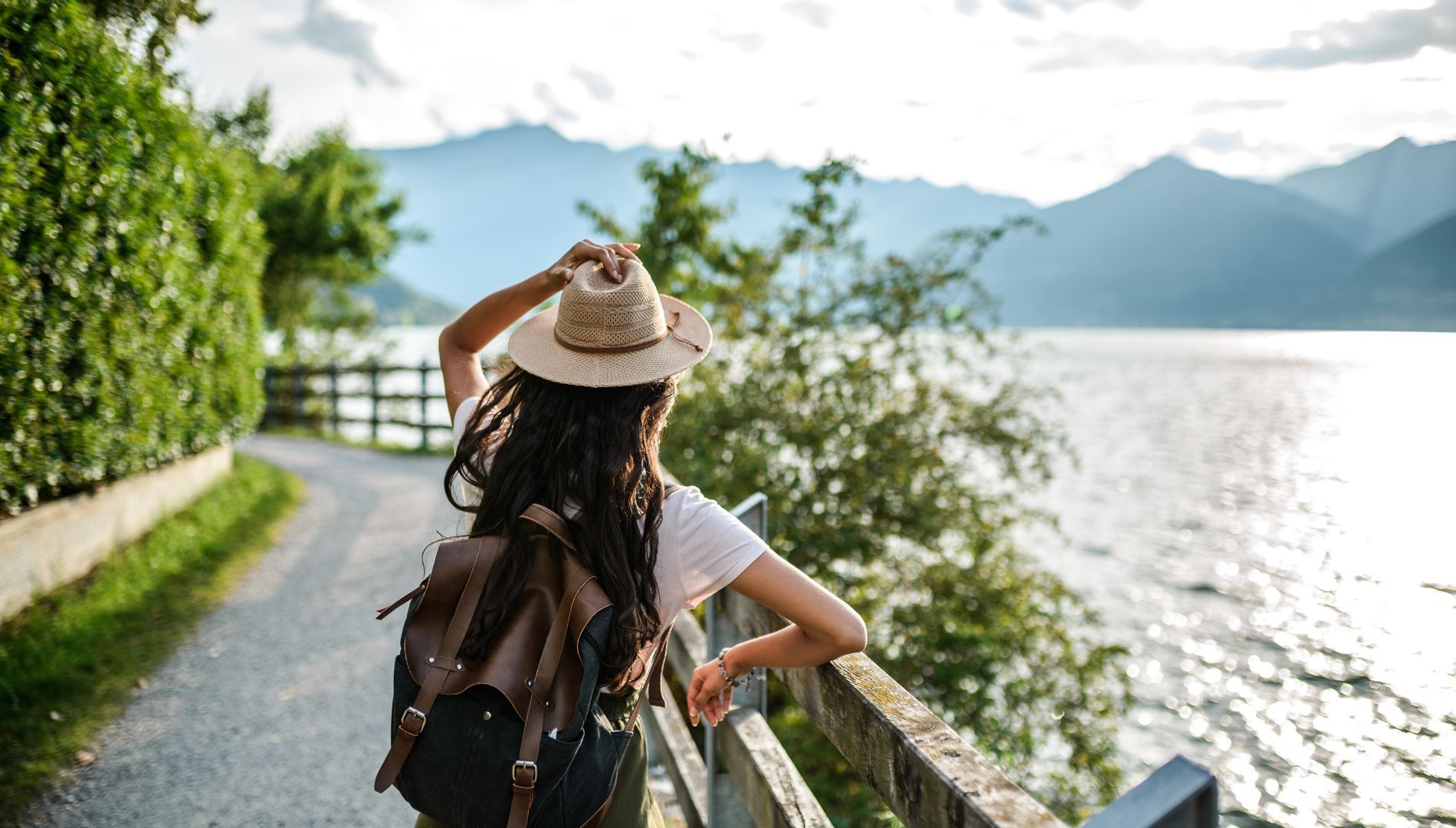 A woman with a backpack is standing on a bridge overlooking a lake.