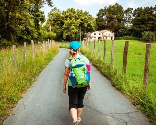 A woman with a green backpack is walking down a road