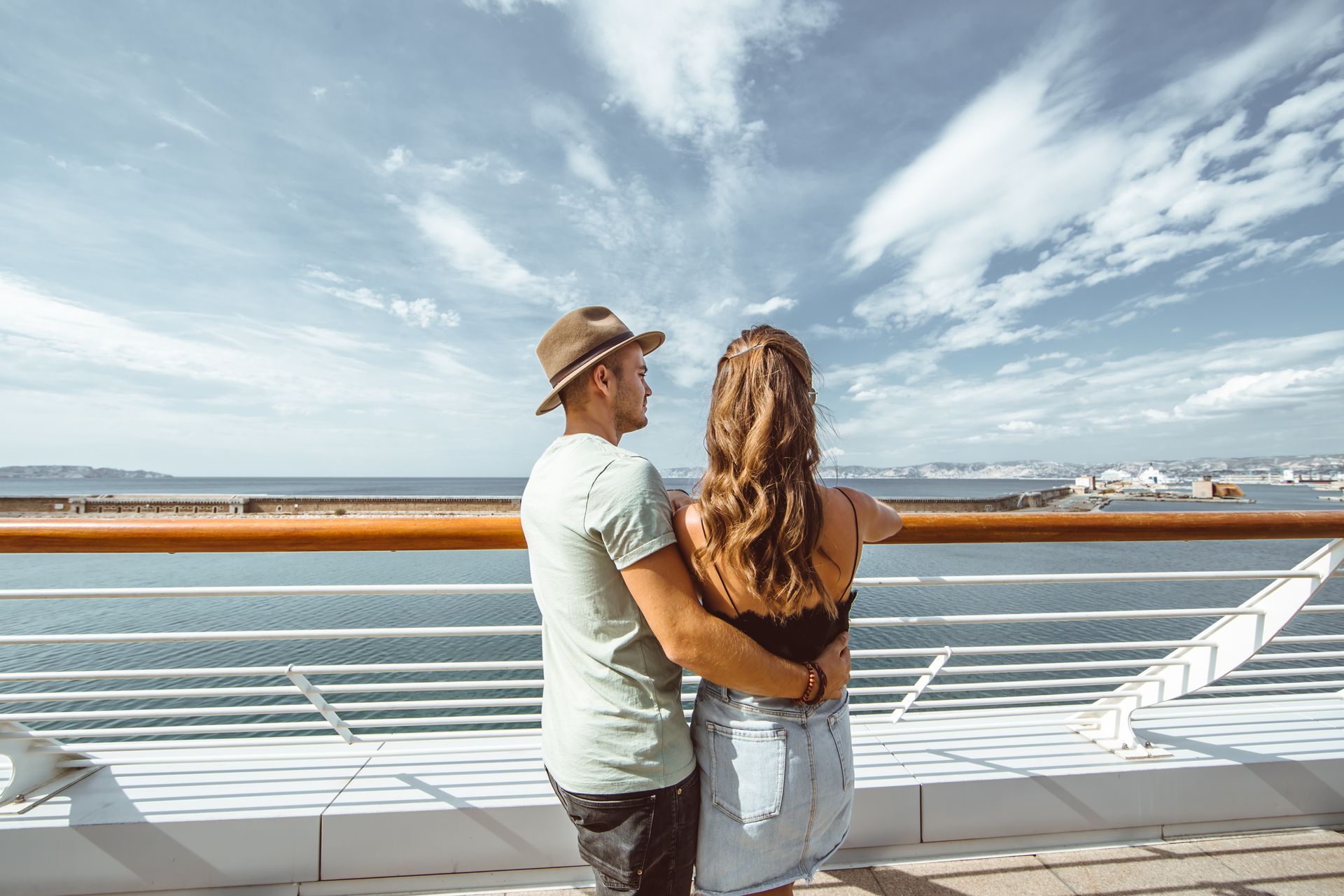 a man and a woman are standing on a cruise ship looking out over the ocean .