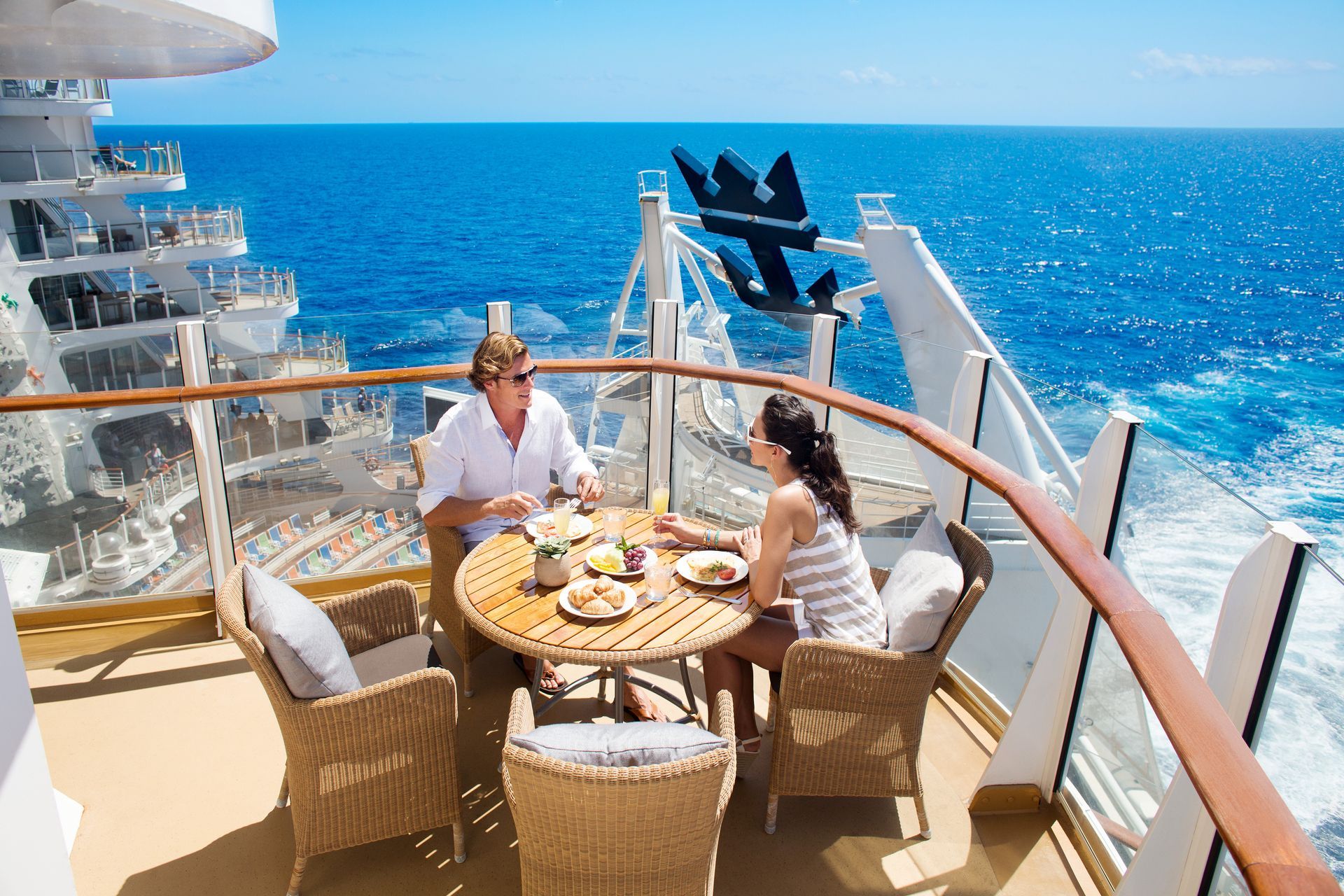 a man and a woman are sitting at a table on a balcony on a cruise ship.