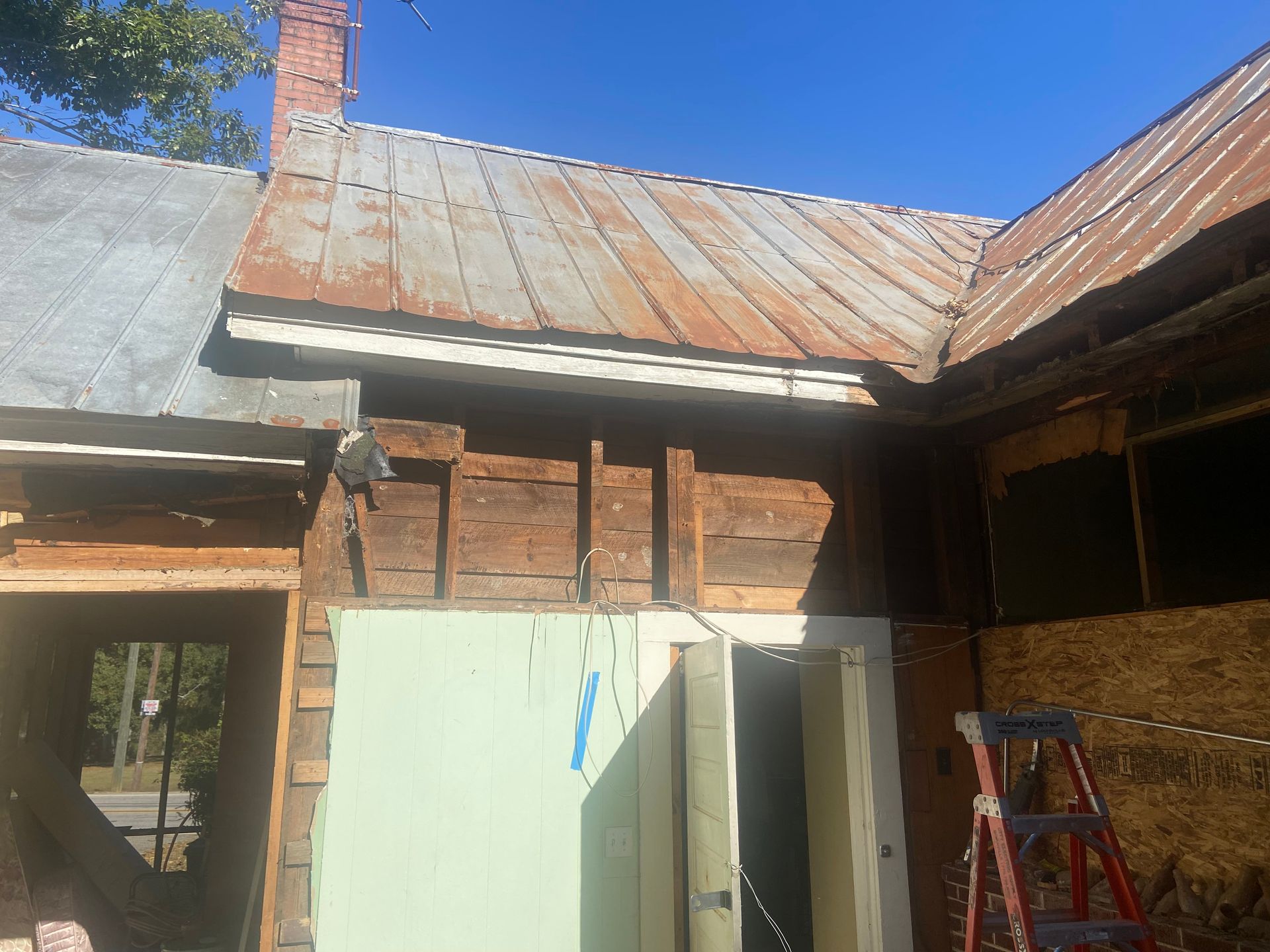 Old wooden building with rusty metal roof, doorway, and ladder.