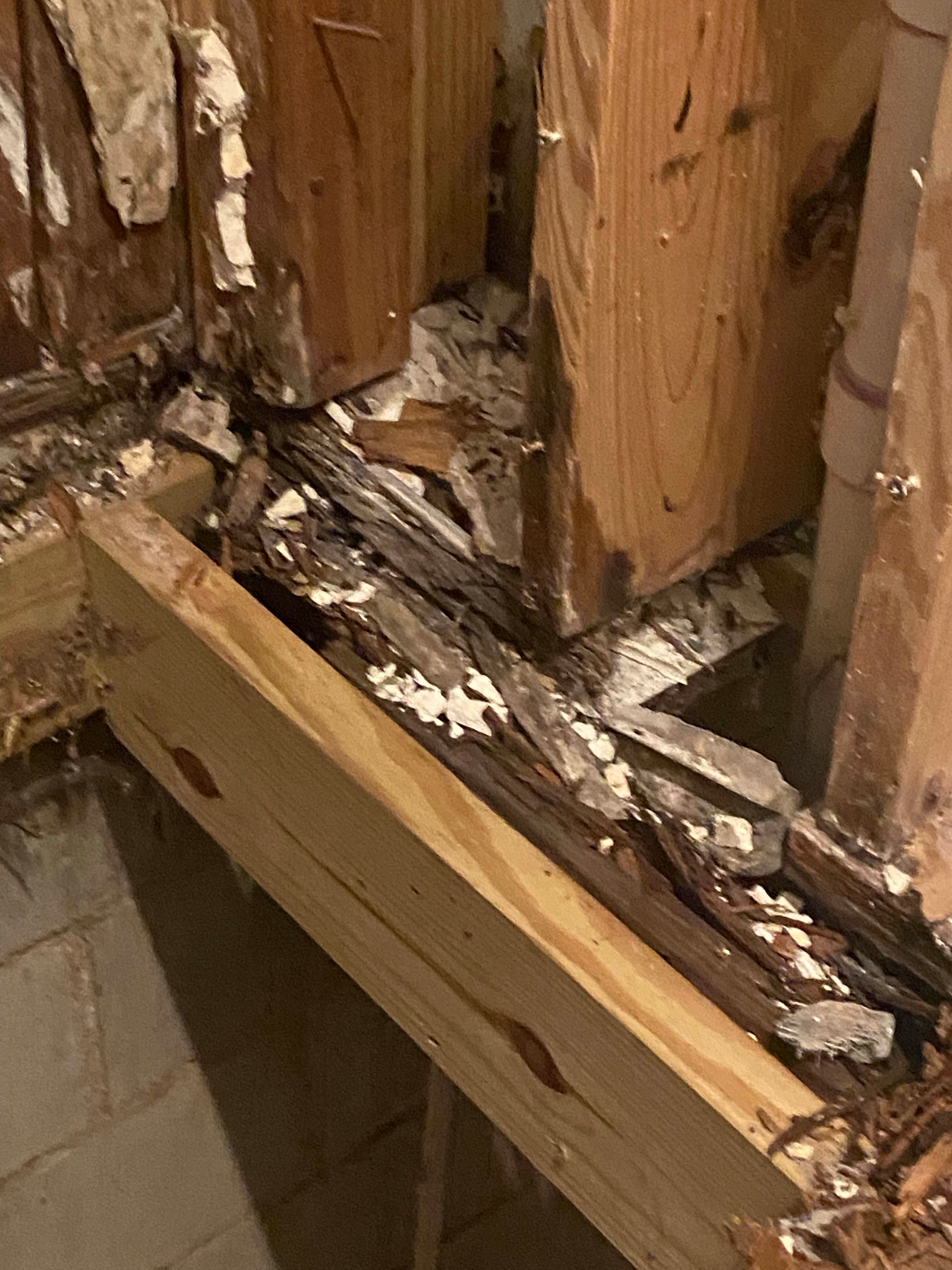 Damaged wood framing with rotted planks and crumbling debris in a wall, likely water damage.