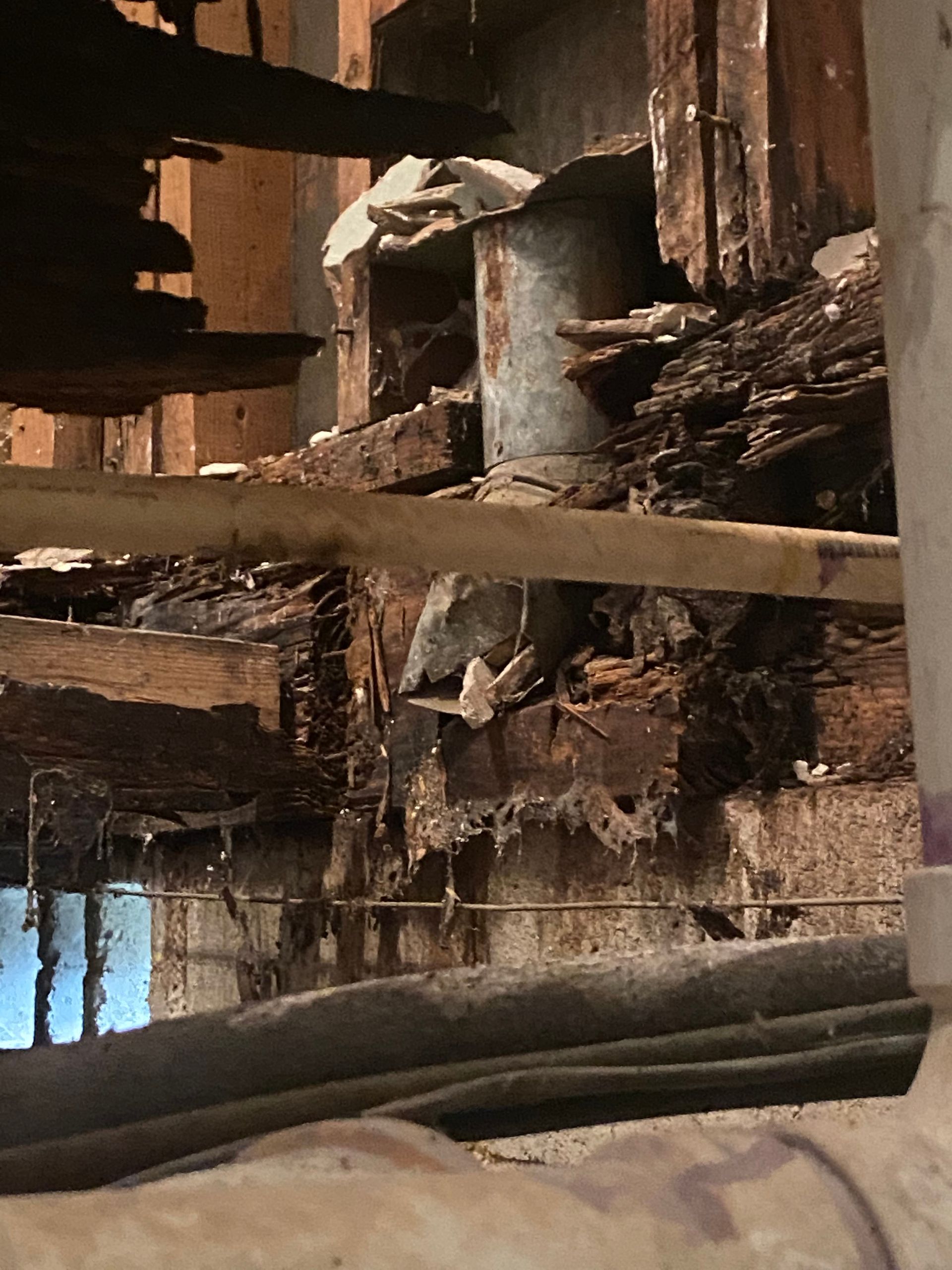 Severely damaged wooden wall with exposed beams, deteriorated by water and age.