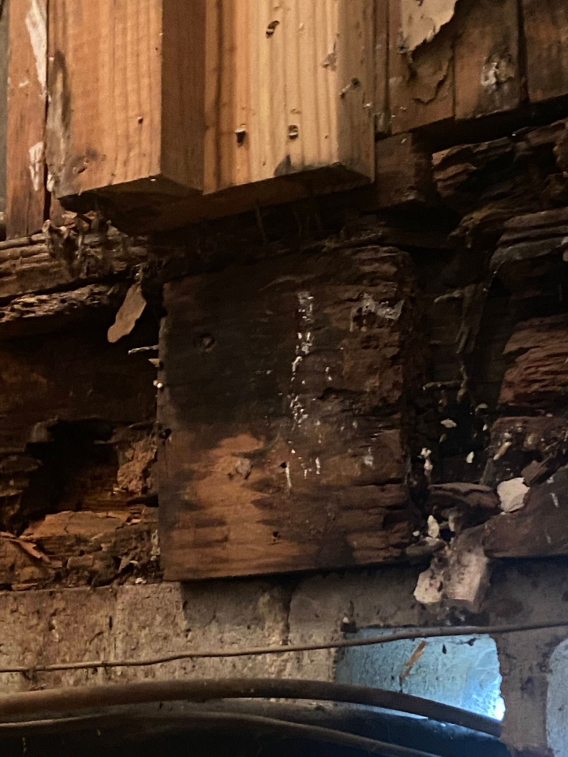 Wood beam construction with significant rot damage, visible against a dark background.