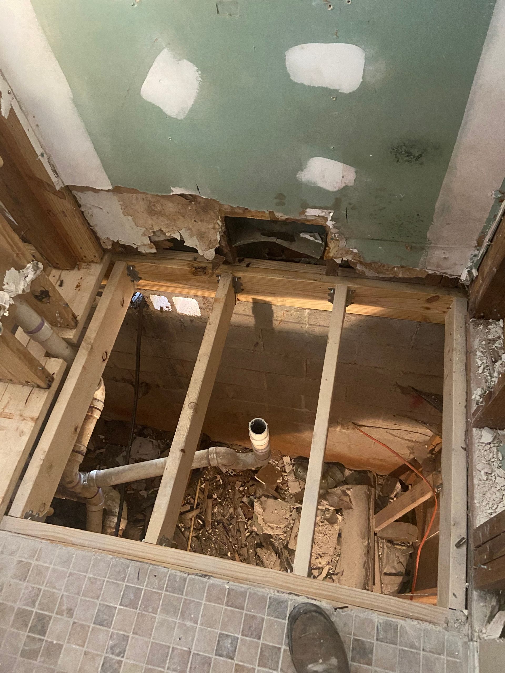 Bathroom floor under renovation, revealing subfloor and framing. Damaged plaster ceiling, tile floor visible.