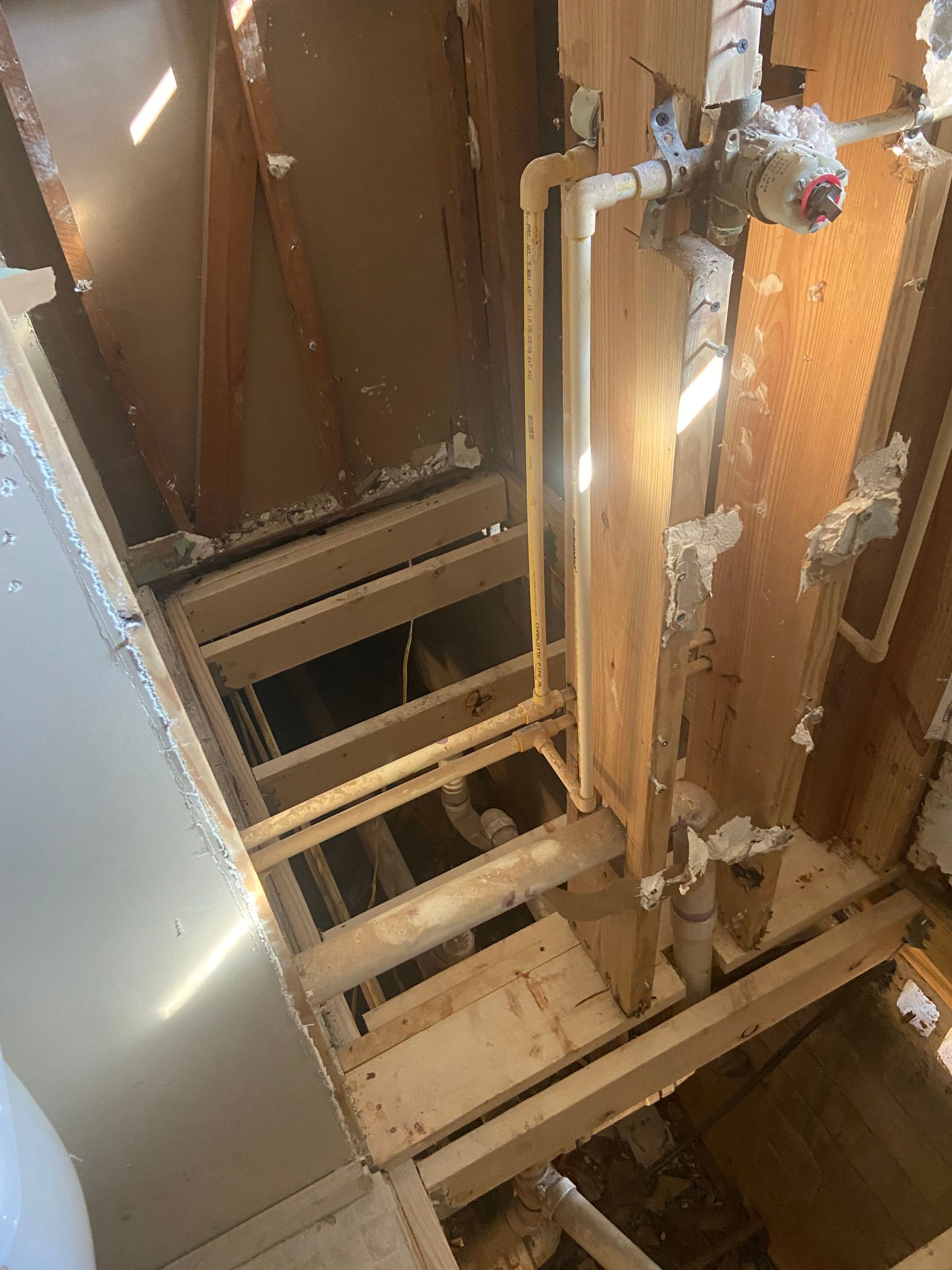 Bathroom under construction; exposed framing, pipes, and damaged walls; sunlight streams in.